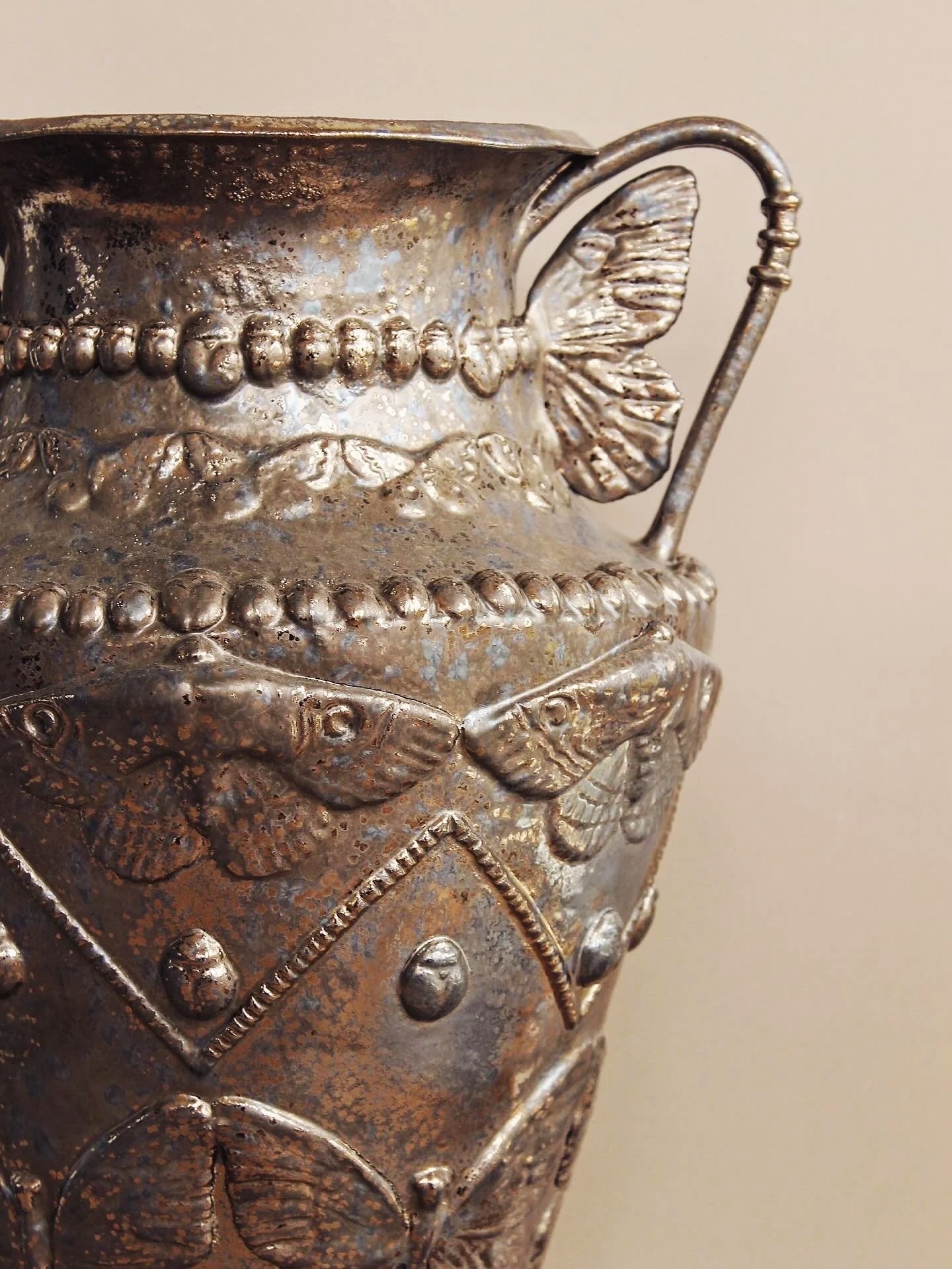 Close-up of a metallic decorative vase with embossed butterflies and beaded borders.