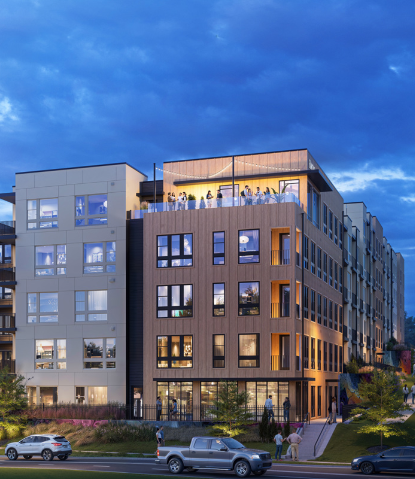 Modern multi-story apartment building with large windows and a rooftop patio with people gathering, set against a cloudy evening sky.