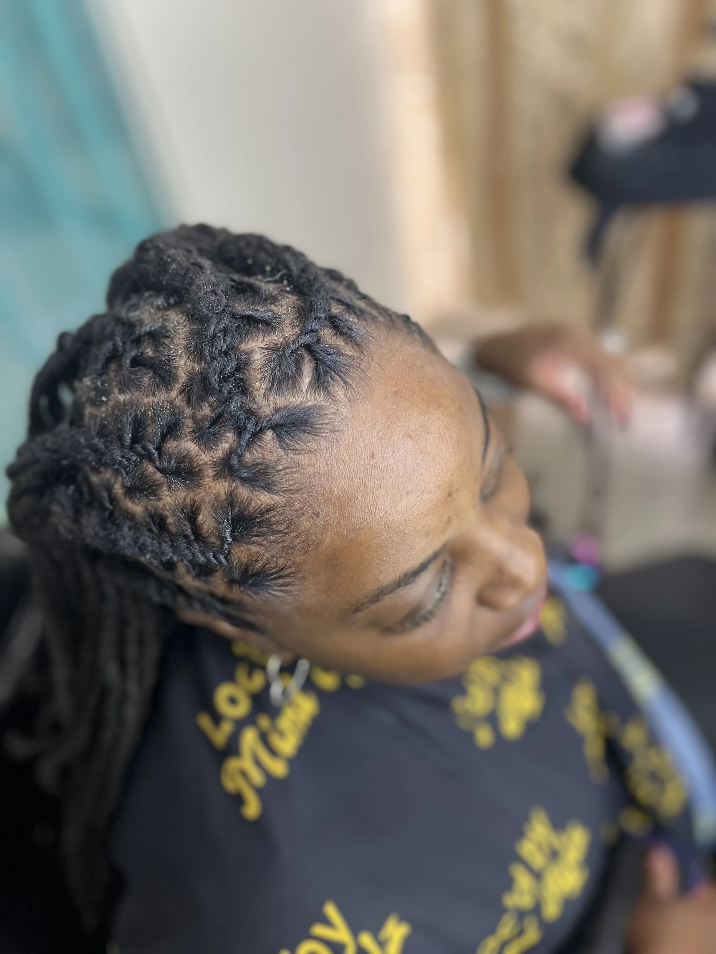Close-up of a person's head with neatly styled, curled black hair, showing the scalp and hair roots.