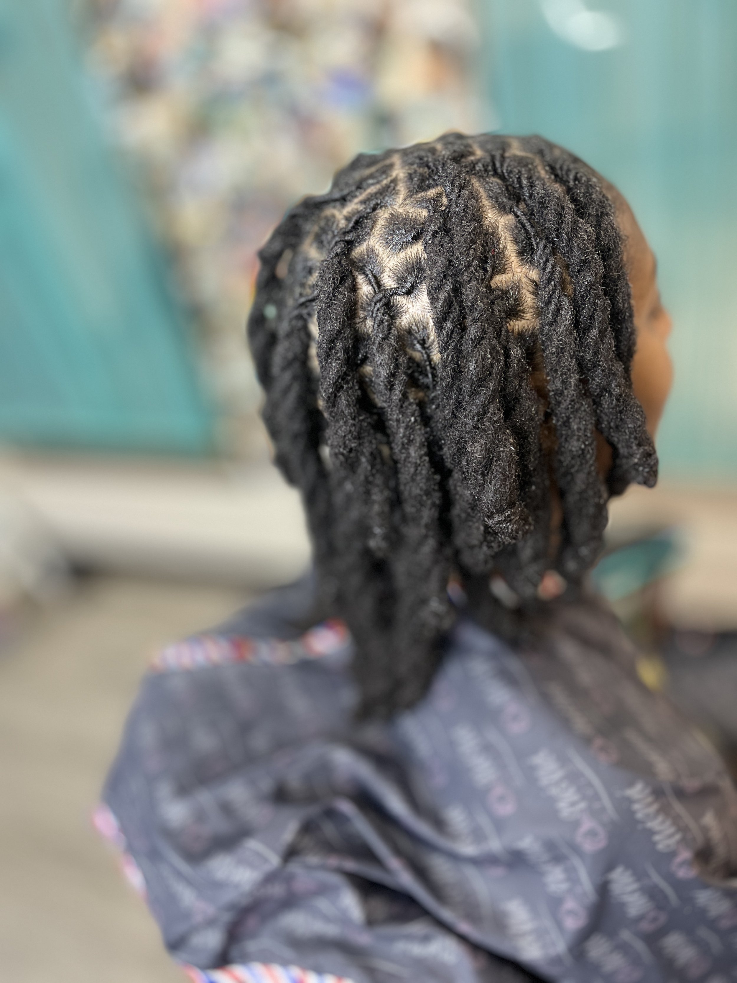 Close-up image of a person with black dreadlocks sitting, with blurred background.