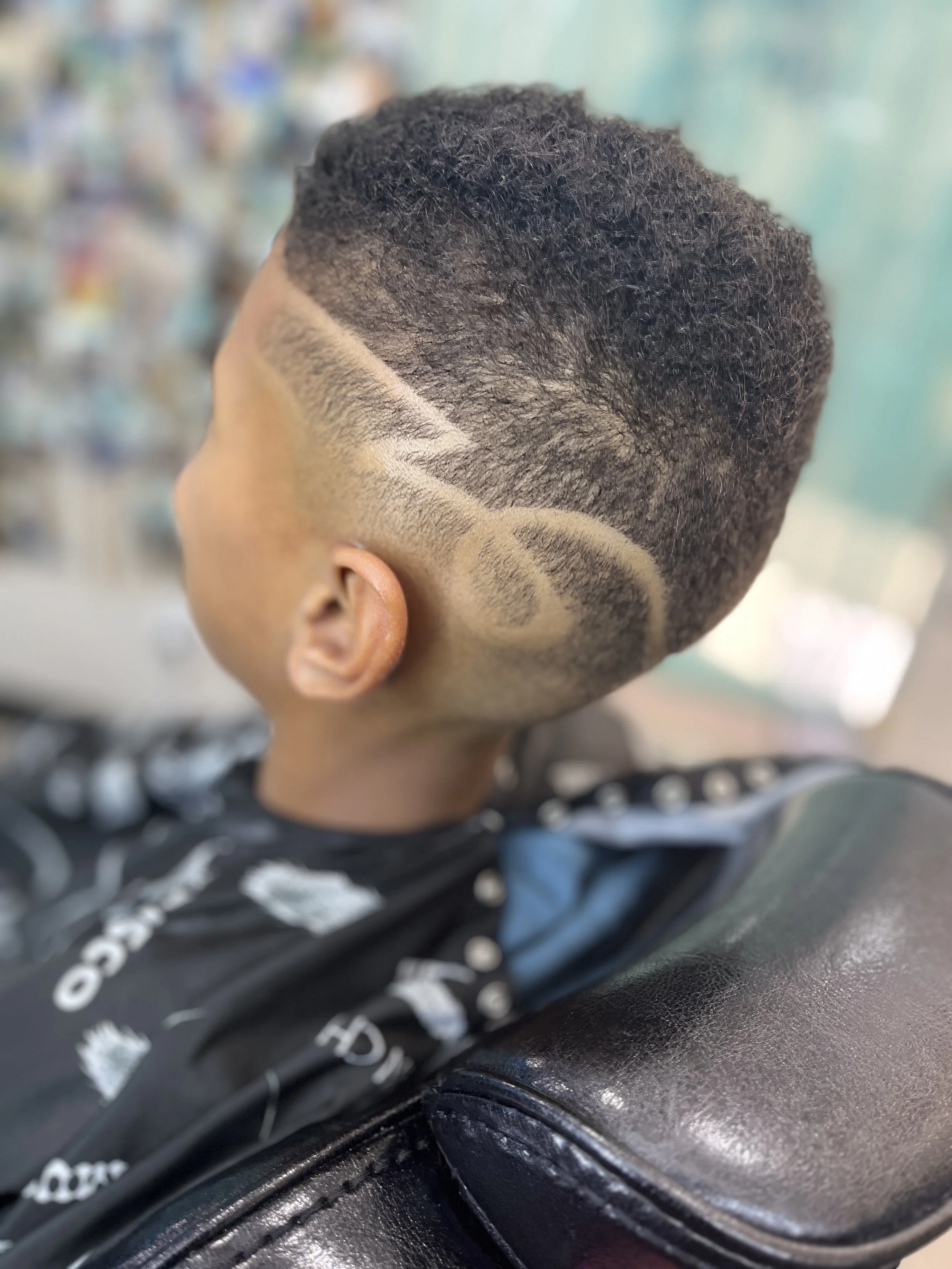 Close-up of a child's haircut with a fade and curved design shaved into the side.