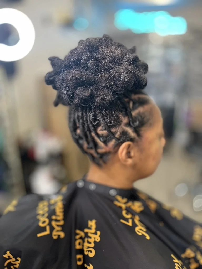 A woman with a short fade haircut and a large, curly hair bun on top, at a salon.