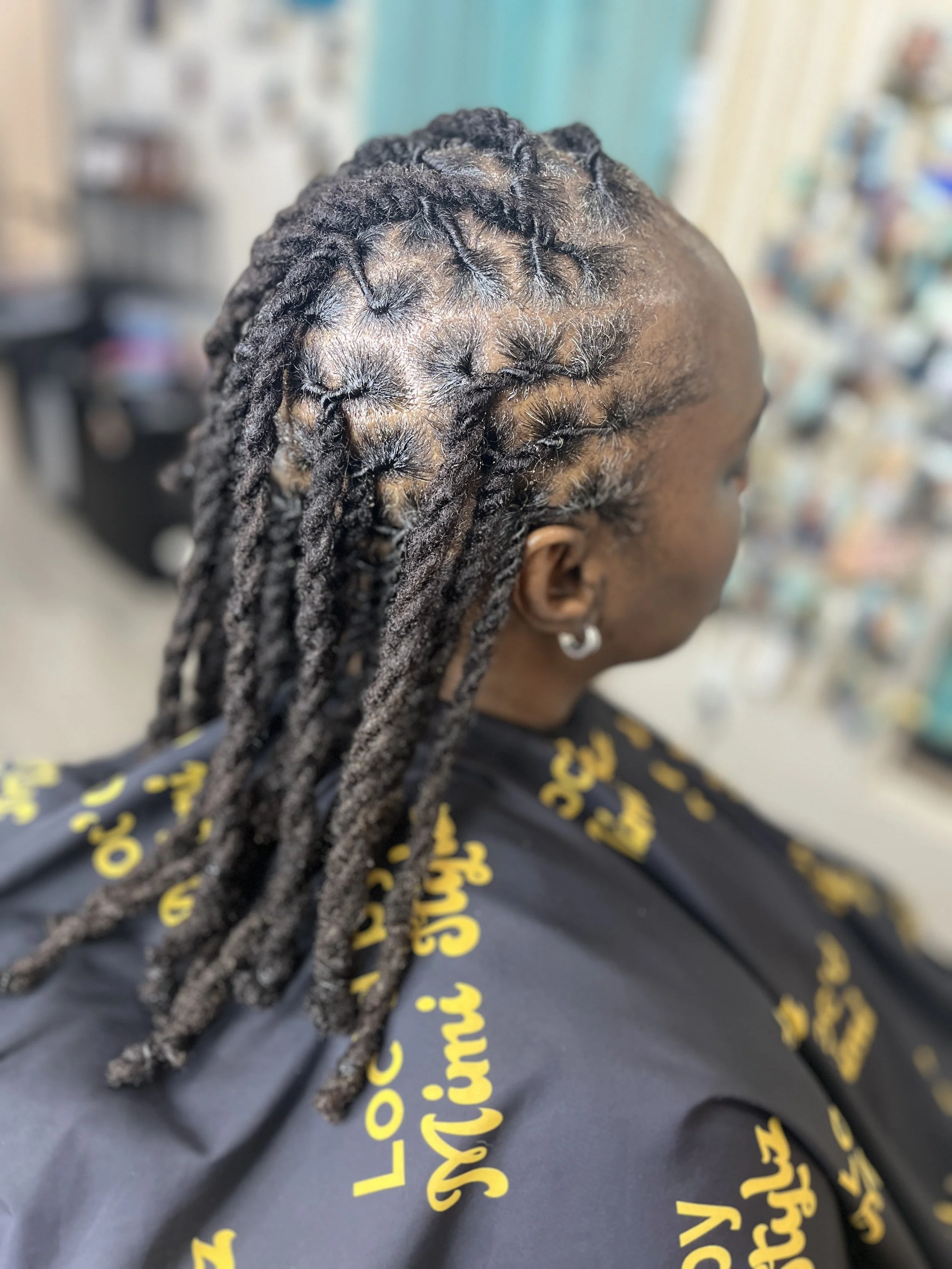 Close-up of a person's head with dreadlocks, some styled into star-shaped sections, in a hair salon setting.