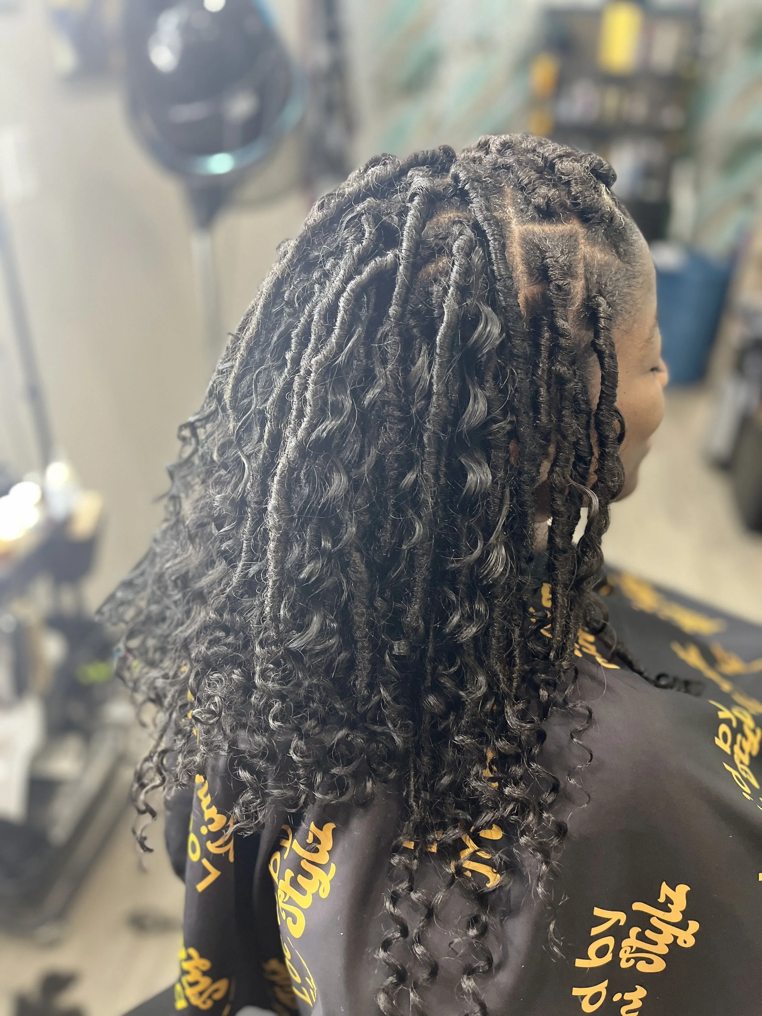 Close-up of a person's head with styled, curly, black hair featuring twists and curls, in a salon or barbershop setting.
