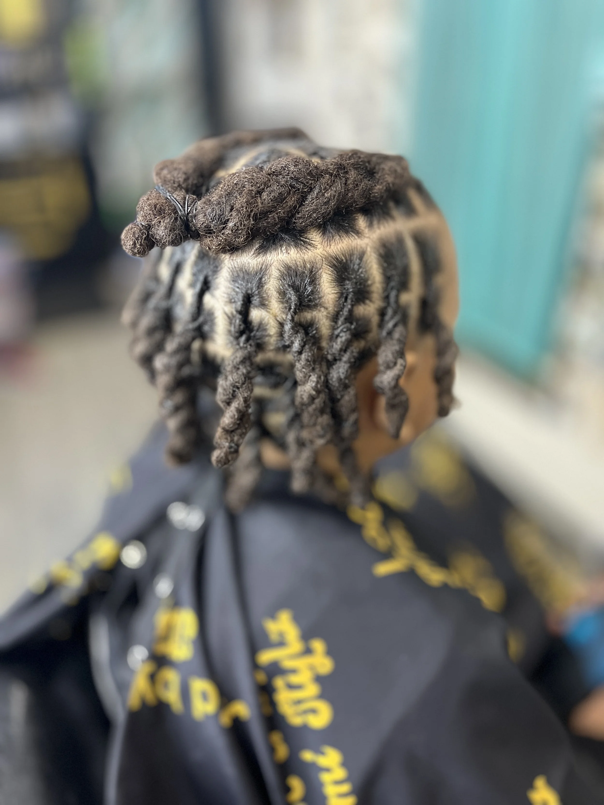 Close-up of a person with gray dreadlocks, wearing a black hoodie with yellow text, in a blurred setting.