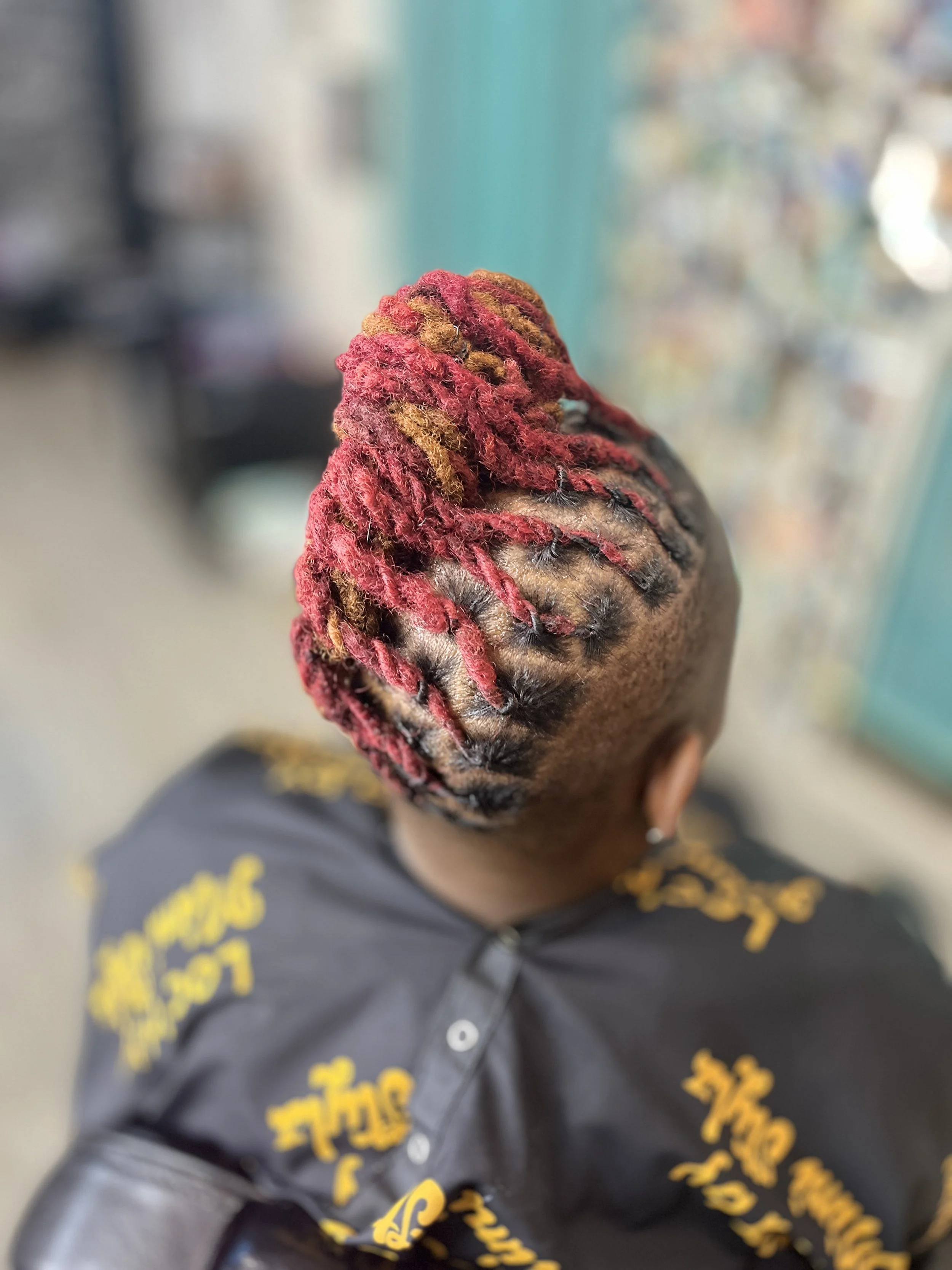 Back of a person's head with red and yellow dreadlocks, wearing a black hoodie with yellow text.