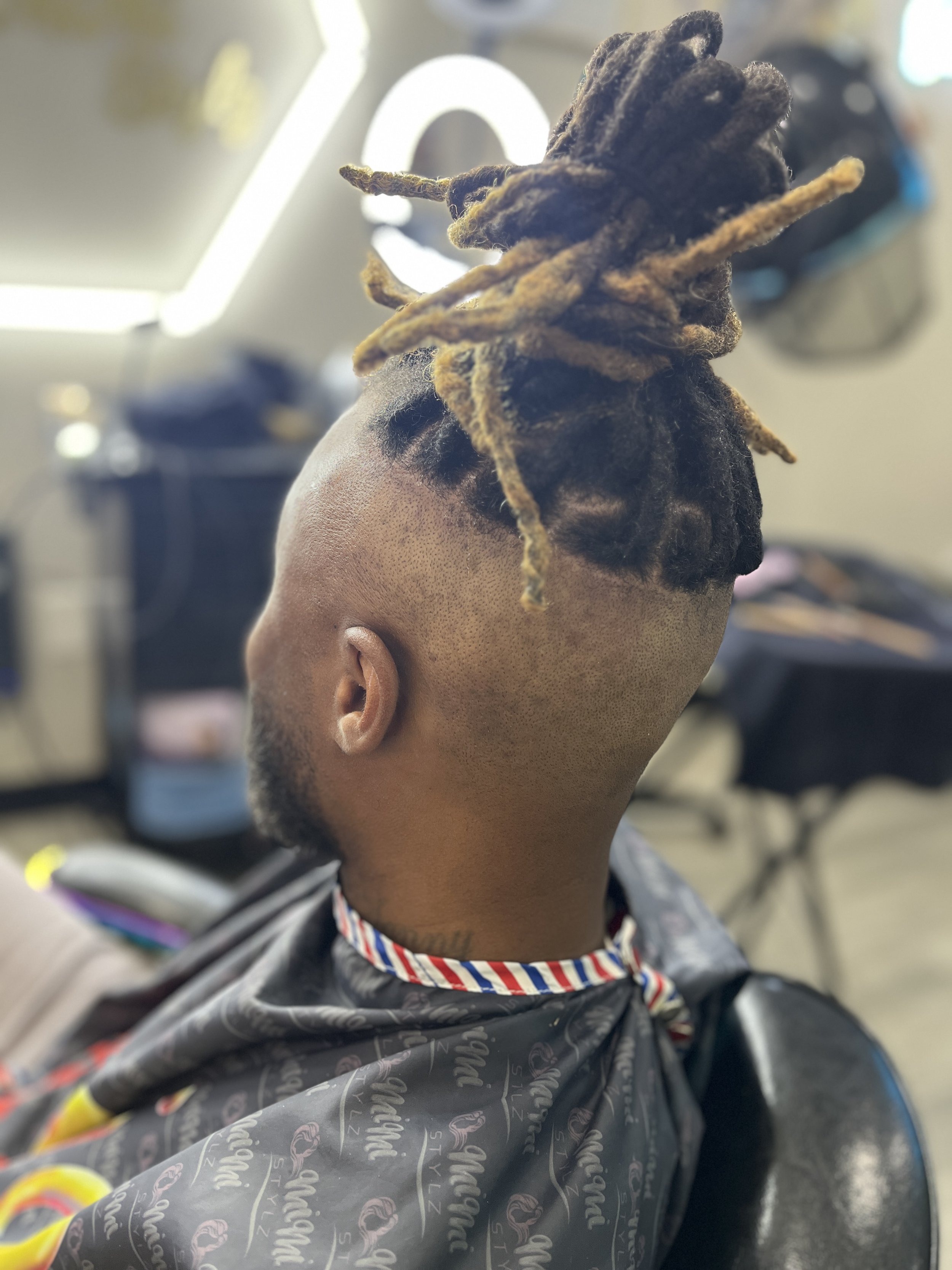Person with short hair and dreadlocks sitting in a barber's chair at a barbershop.