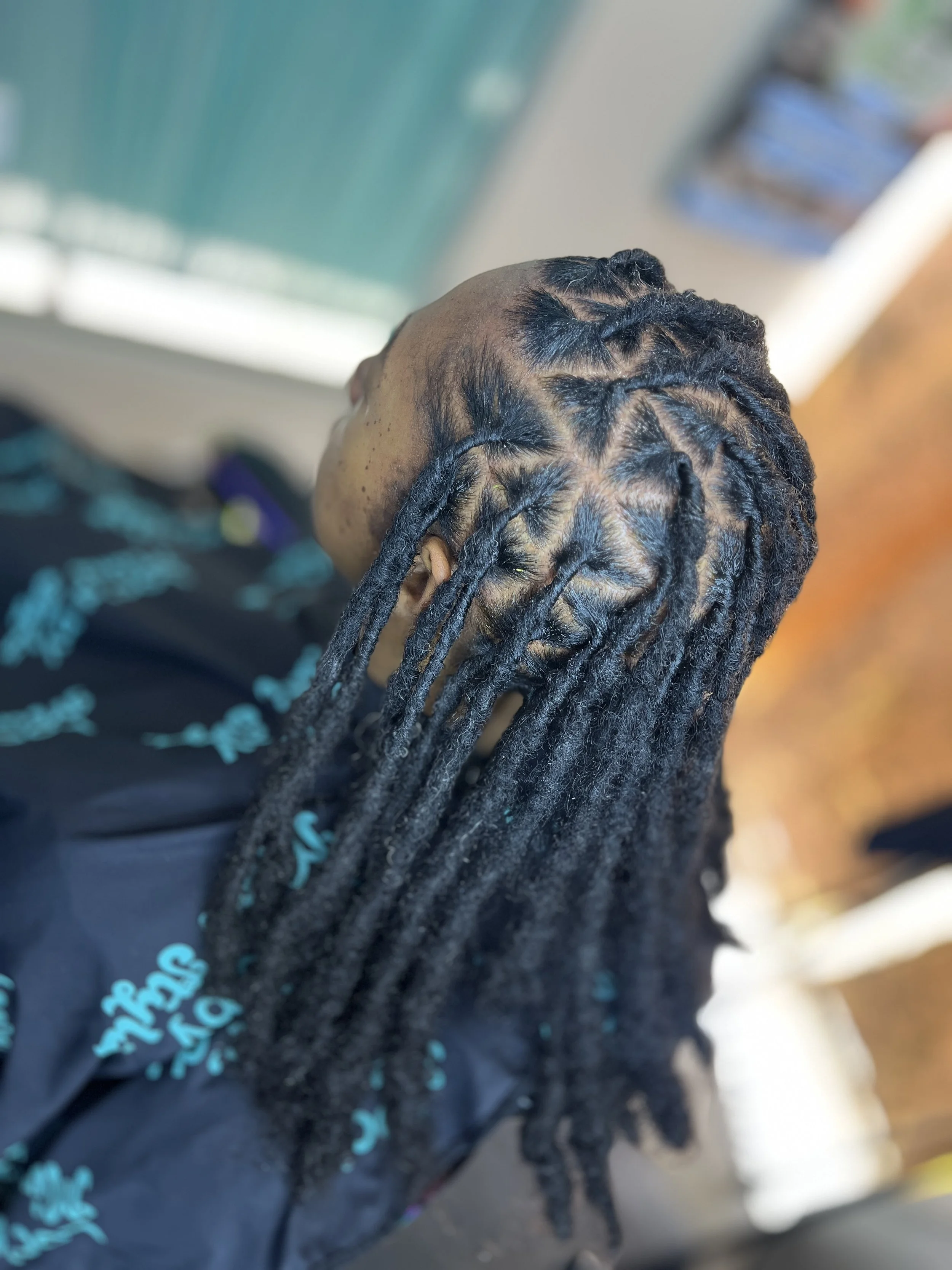 Close-up of a person with dreadlocks, showing the back of their head, wearing a black shirt with teal text.