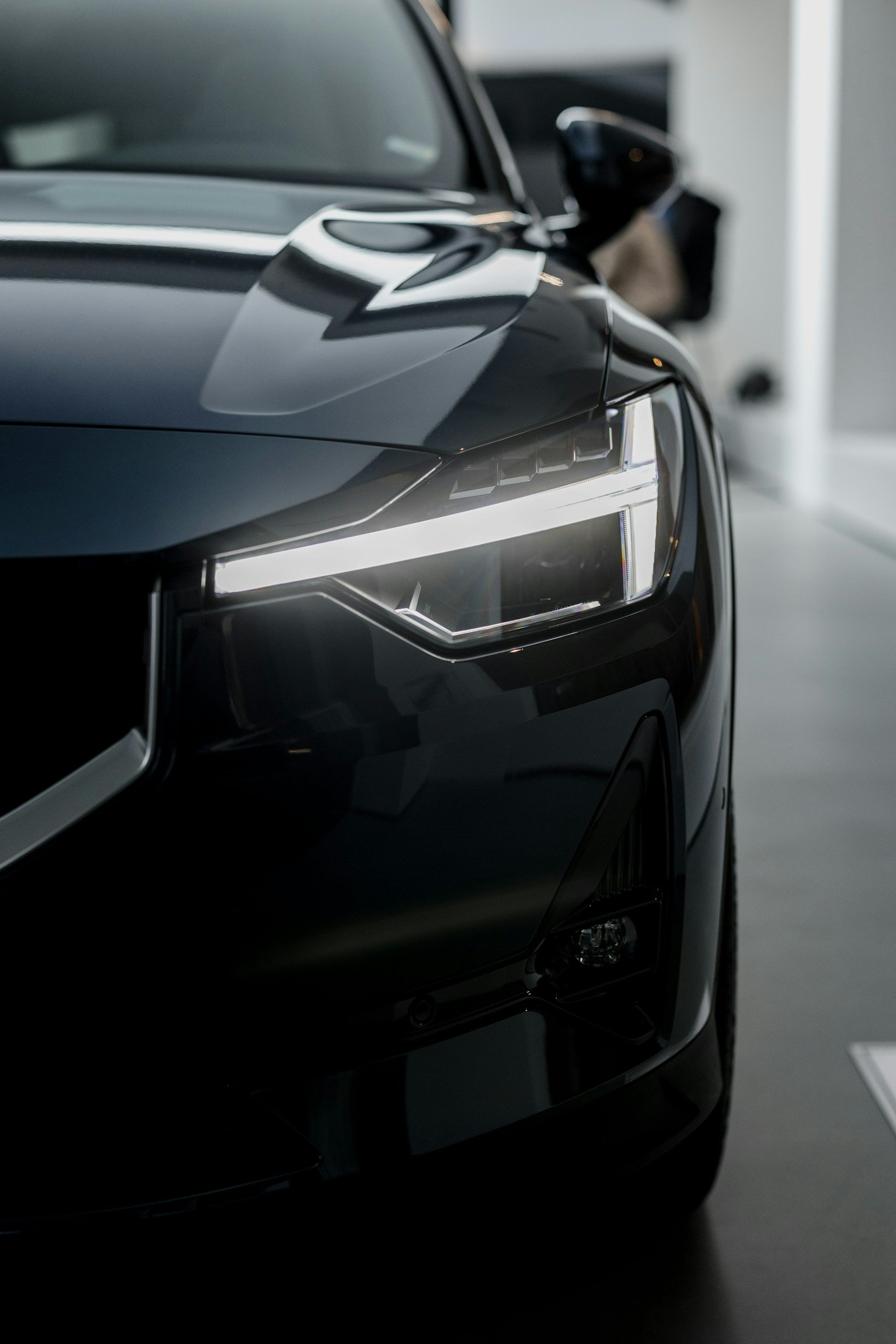 Close-up of the front left side of a sleek black car with modern headlights, parked indoors.