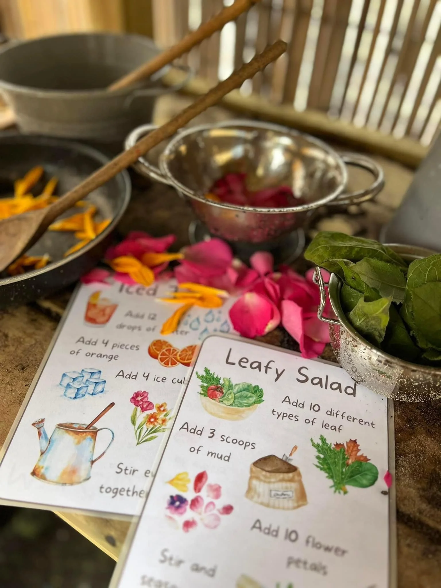 A close-up of a table with flower petal and leaf salad recipes, bowls with flower petals, a colander with leafy greens, and a woven background.