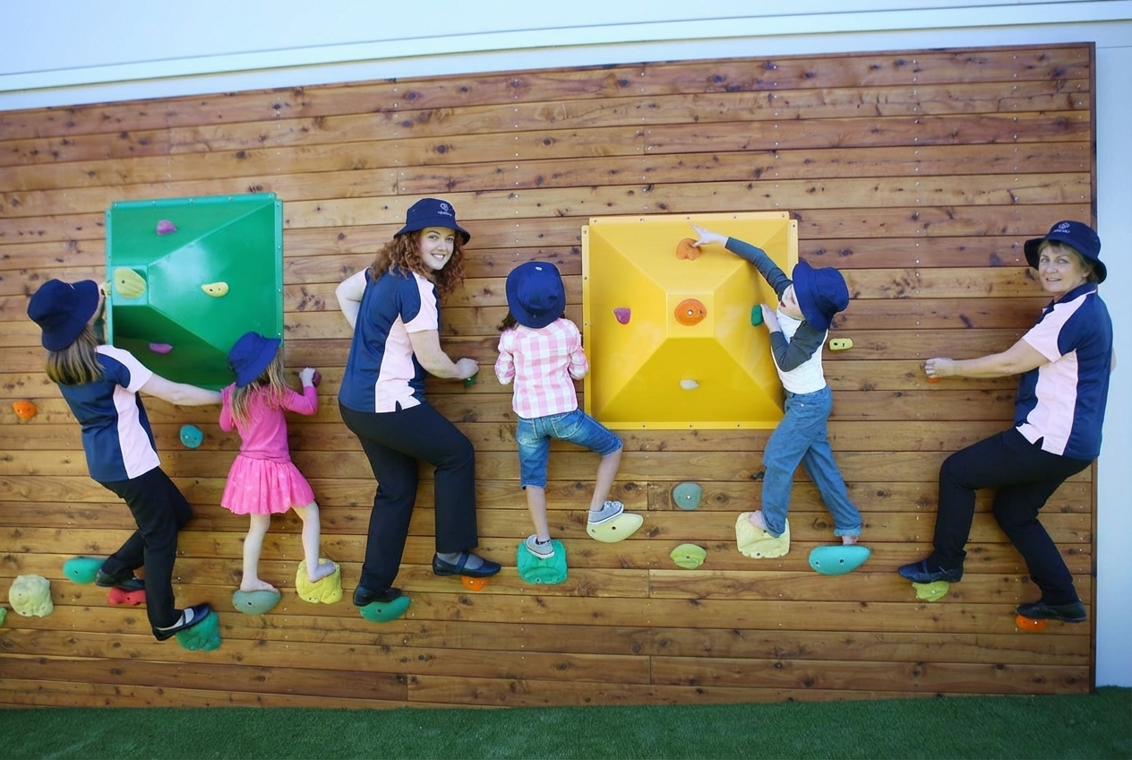 Children and adults climbing on an indoor rock wall with colorful holds and a wooden background