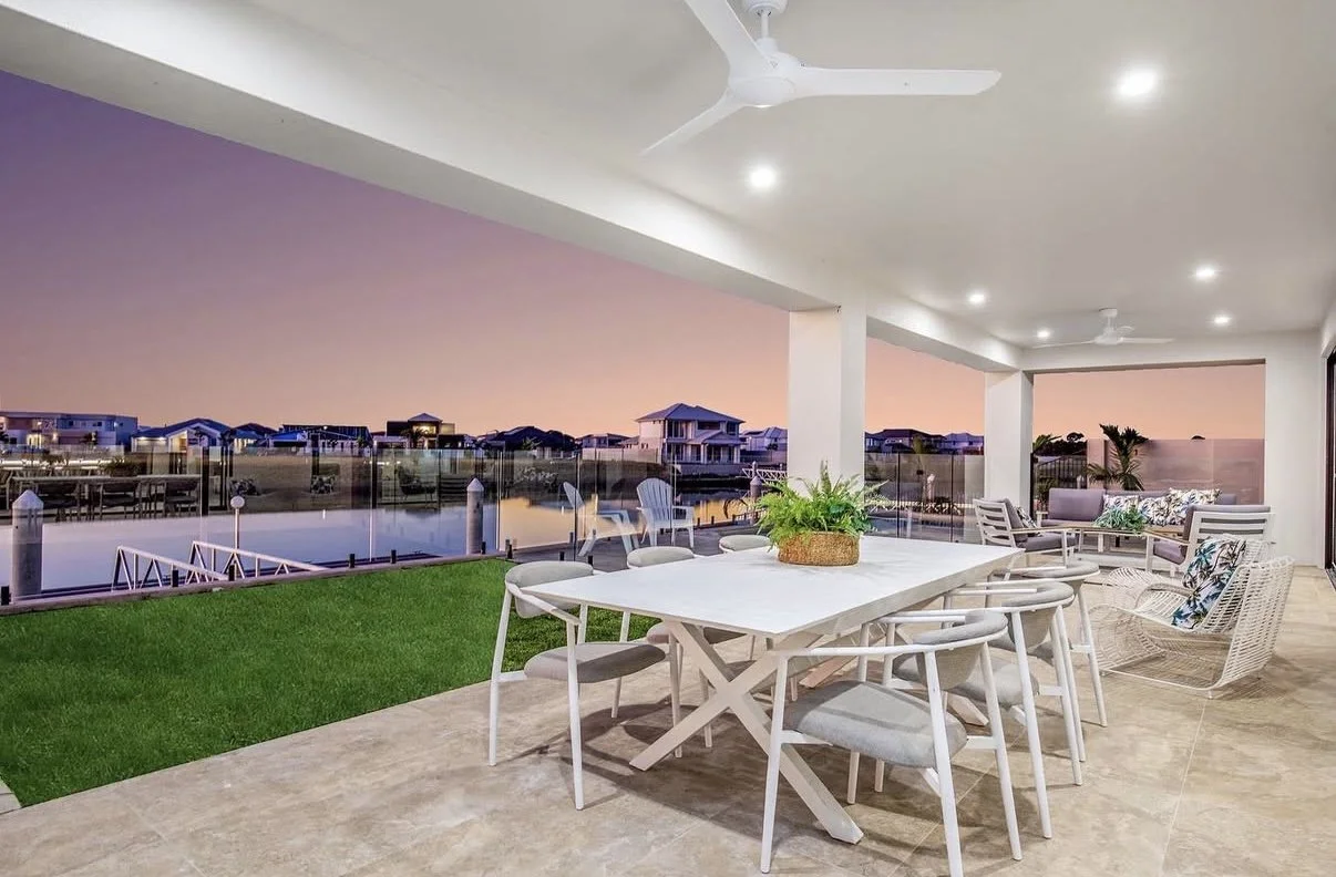 An outdoor patio with a dining table, chairs, and patio furniture, overlooking a waterway at sunset.