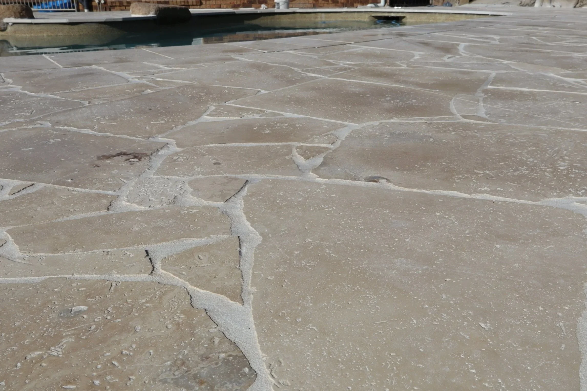 A close up image of a kidney shaped backyard pool with turquoise water, surrounded by natural stone crazy pave completed by Haven Tiling & Stone Pty Ltd tilers, creating a more natural and luxury designed poolside area.