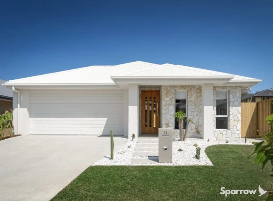 Front view of a modern white house with a garage, stone accents, and a wooden door, set against a clear blue sky.