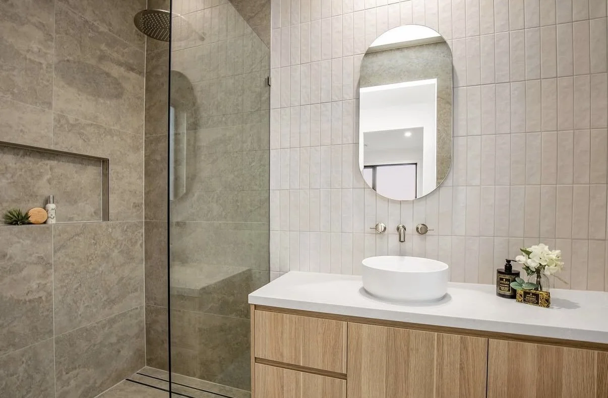 Modern bathroom with a walk-in shower, a white countertop with a vessel sink, a mirror, and decorative accessories.