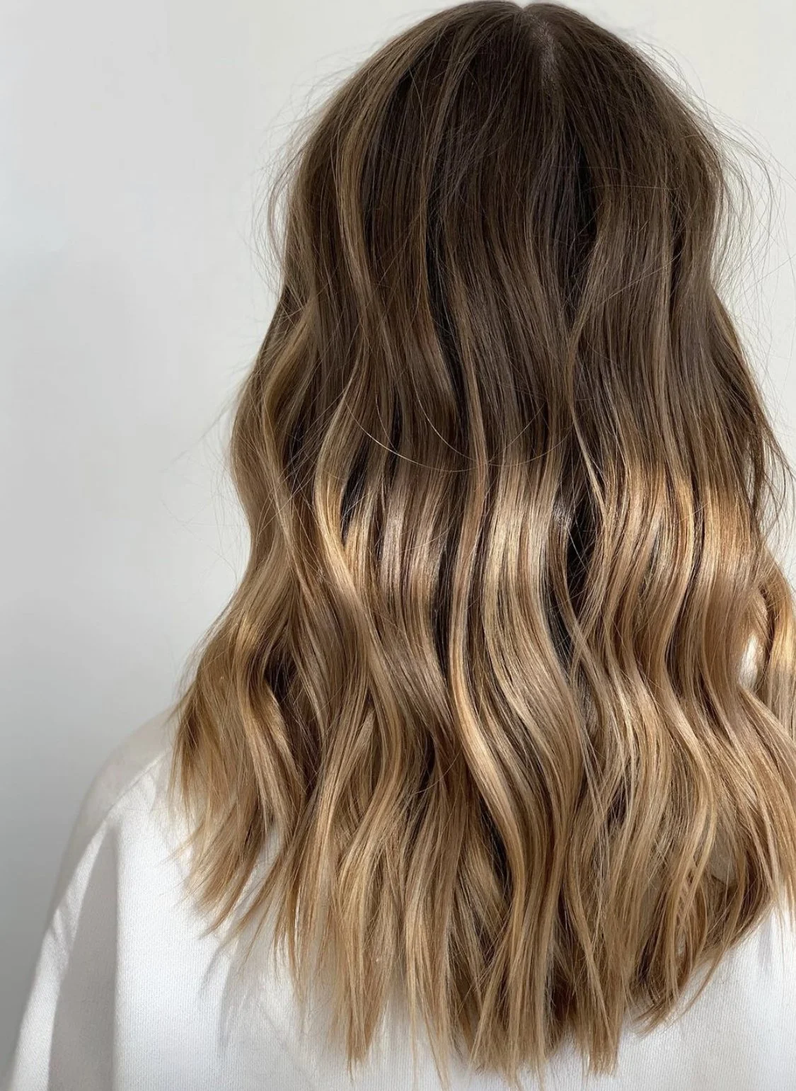 Back view of a woman with long, wavy, light brown hair with blonde highlights.