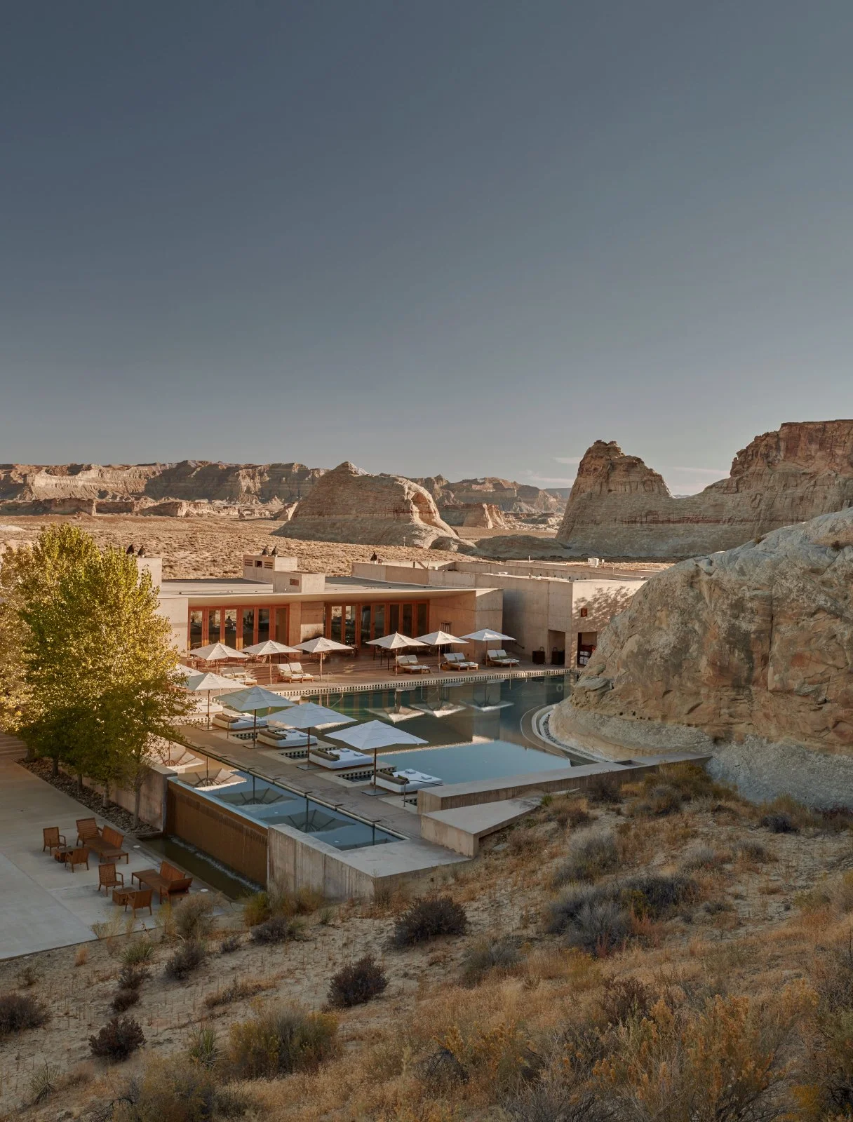 Luxury hotel pool area with lounge chairs and umbrellas surrounded by desert landscape with rock formations.