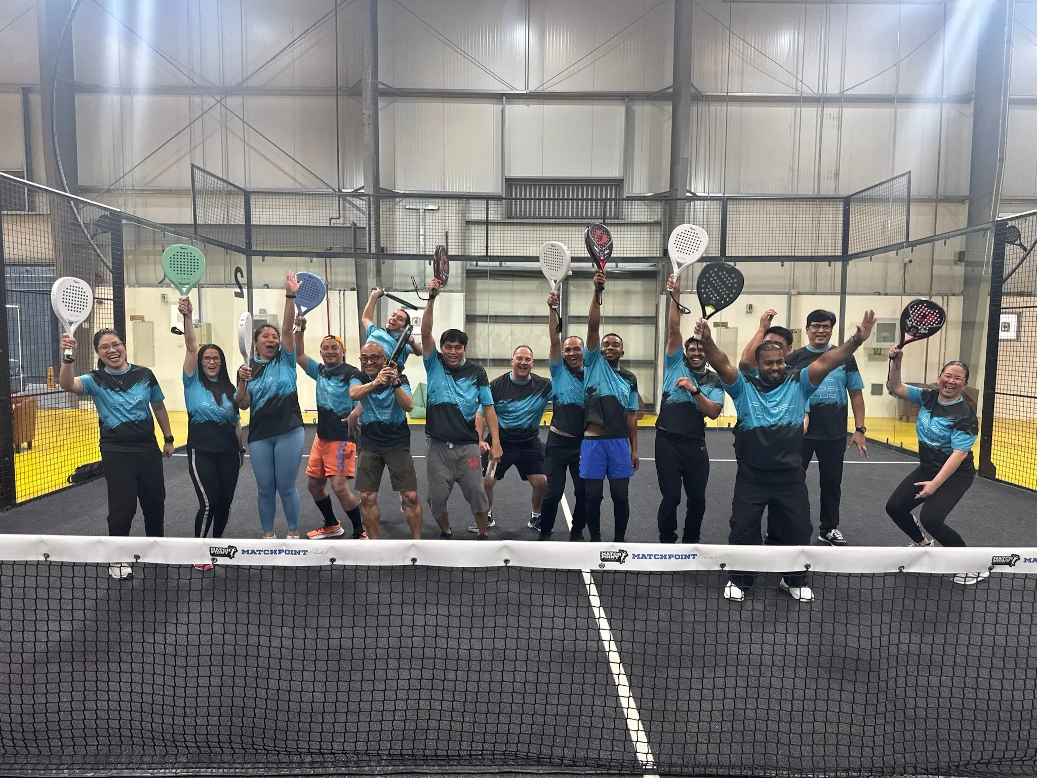Group of people on an indoor padel court holding paddles and smiling.
