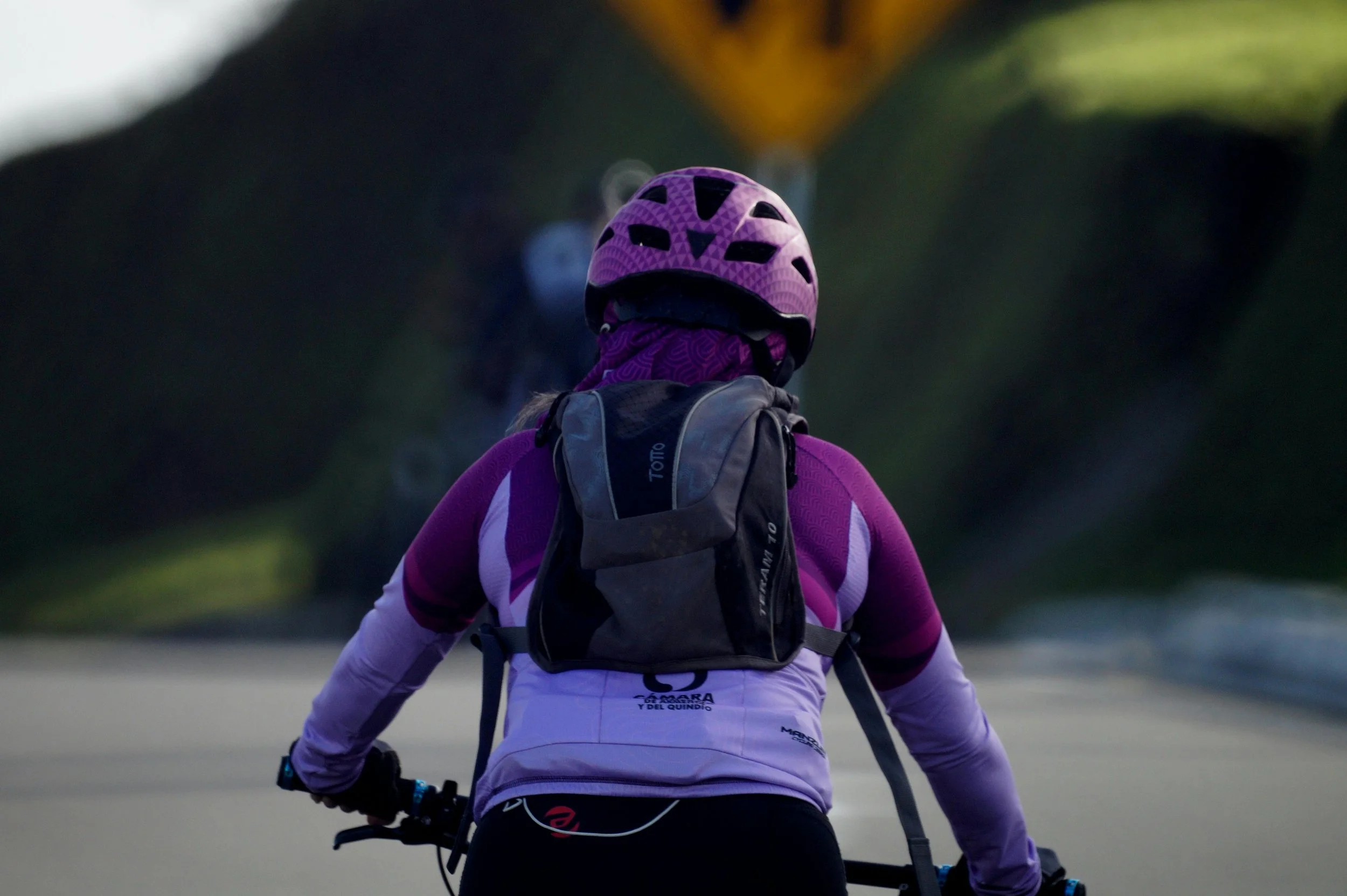 A person riding a bicycle wearing a purple helmet, purple jacket, and carrying a backpack.