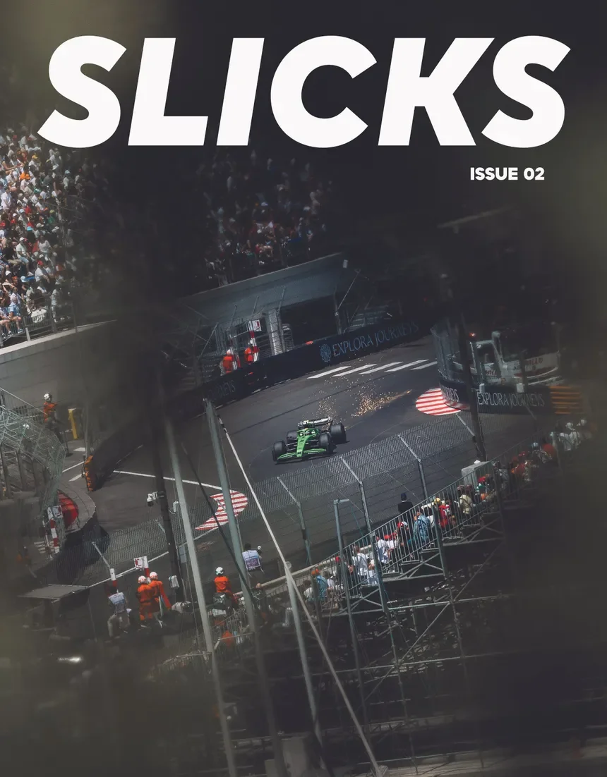 An aerial view of a green race car on a street circuit with spectators watching from the stands and along the fences. The scene appears to be from a street racing event, possibly Formula E or similar motorsport. SLICKS magazine