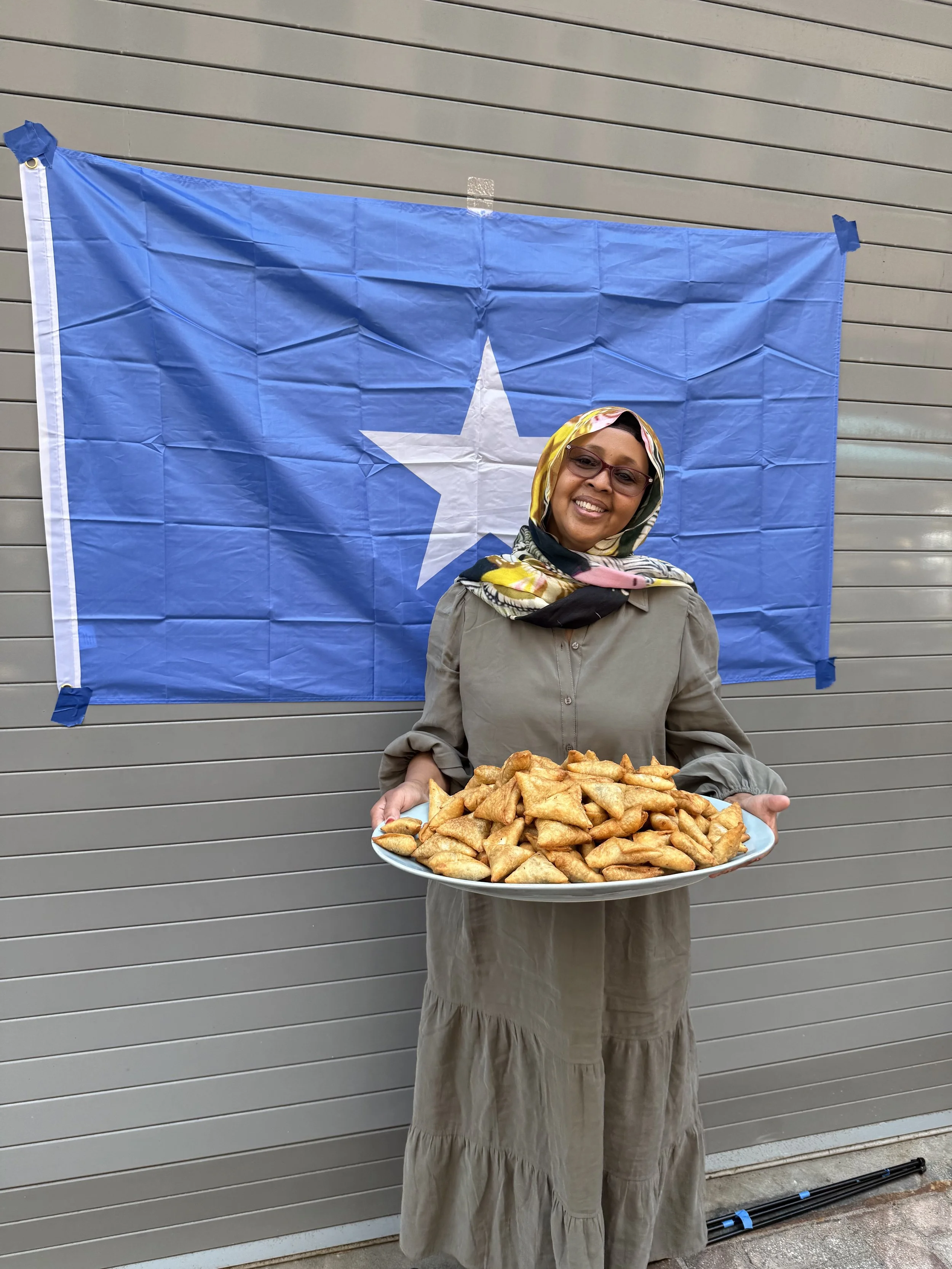 Woman wearing glasses and a headscarf holding a large plate of sambusas.