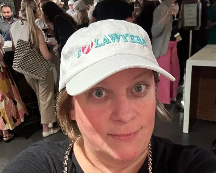 April takes a selfie wearing a hat that says I love lawyers at a networking event.