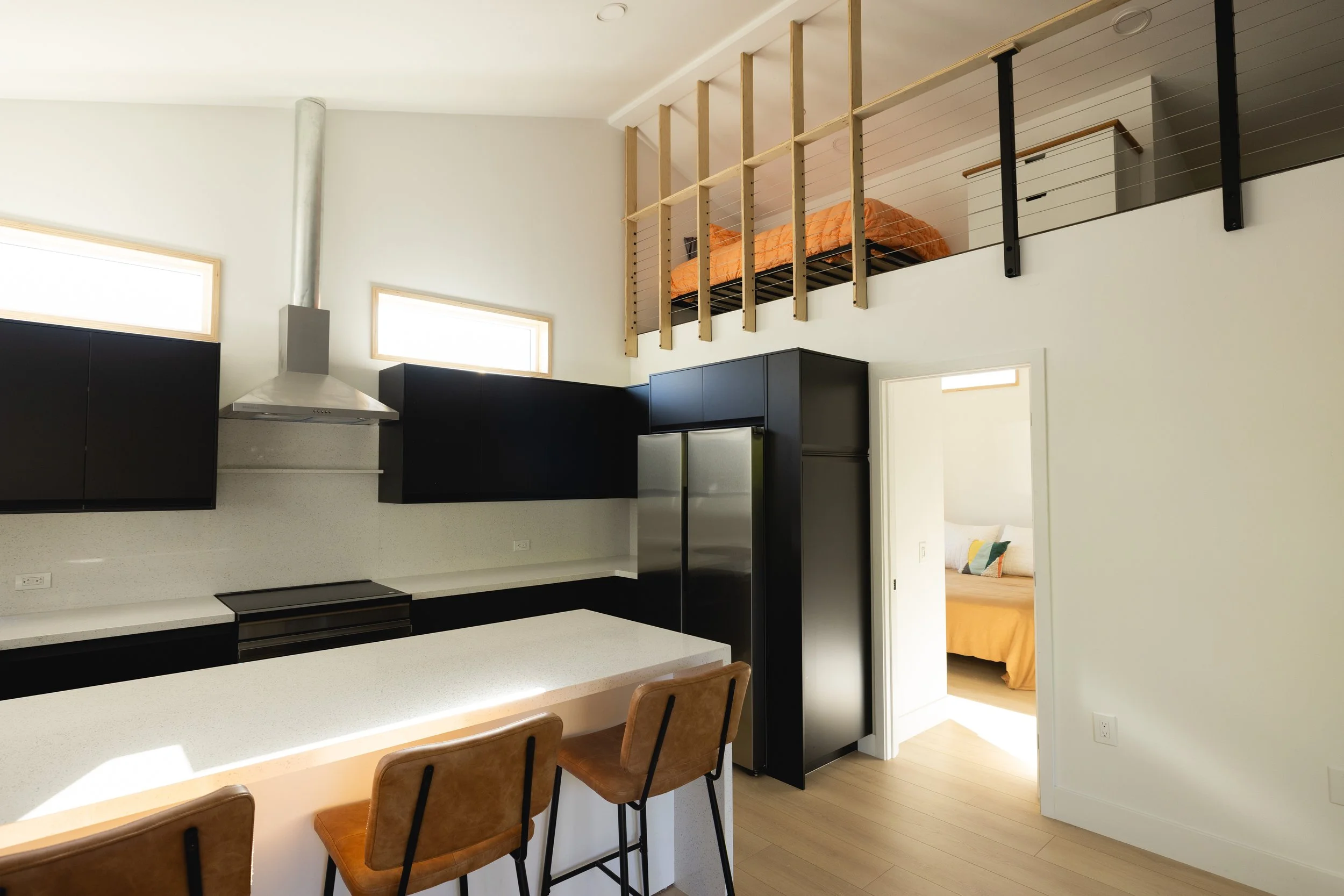 Image of the ADU kitchen and loft space above, and in the background a bedroom is visible with a cozy bed inside