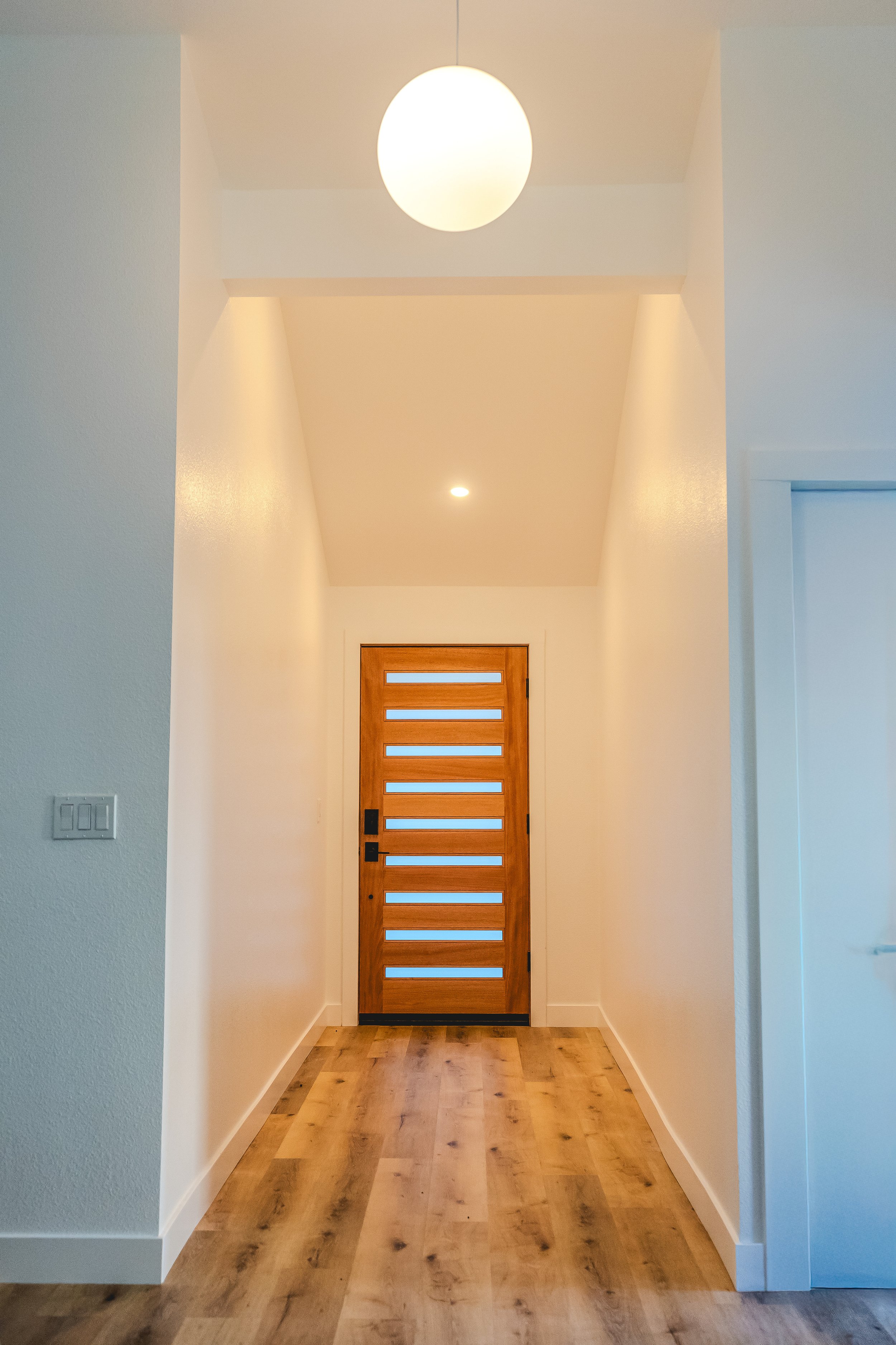 Interior shot of hallway facing the front door. Modern globe light fixture and hardwood front door