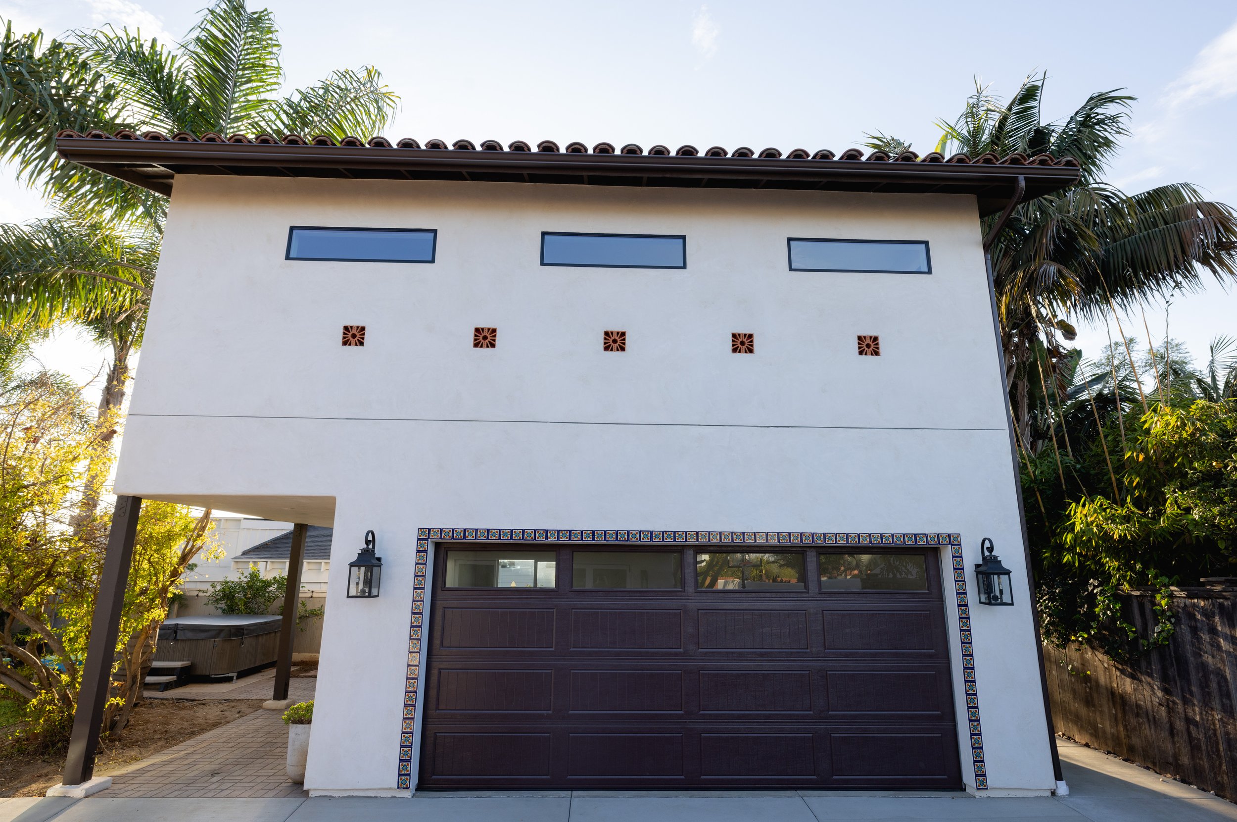 Front of beautiful new Spanish style Casita in Carlsbad, California by Geis Architecture. Creamy white smooth stucco, Spanish tiles surrounding the garage door. Classy, refined, modern, clean. North County, San Diego architecture