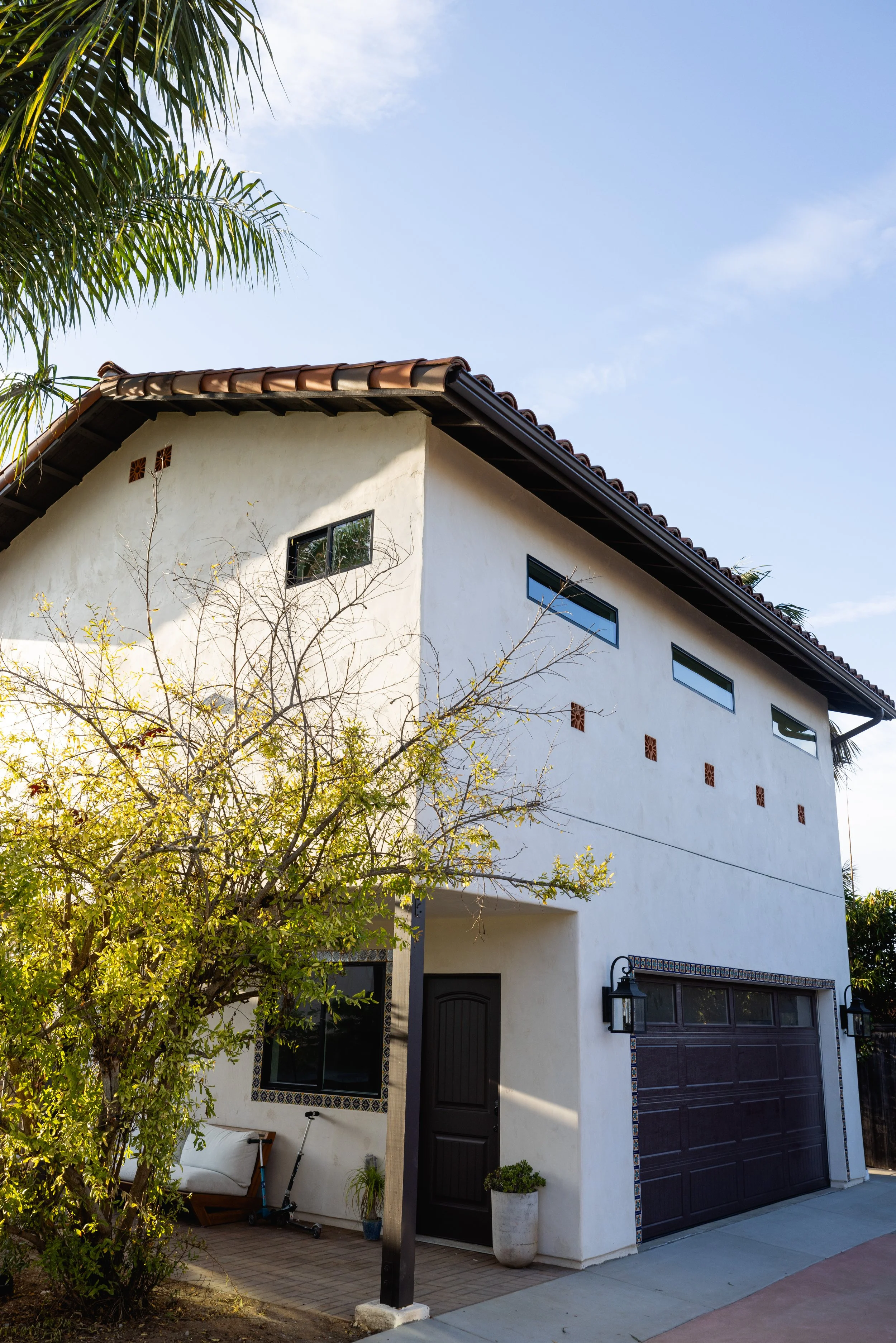 Exterior shot of new ADU build in Carlsbad, California. Spanish style finishes and creamy white smooth stucco with beautiful pomegramate tree blooming on the left. Designed by Geis Architecture in North County San Diego.
