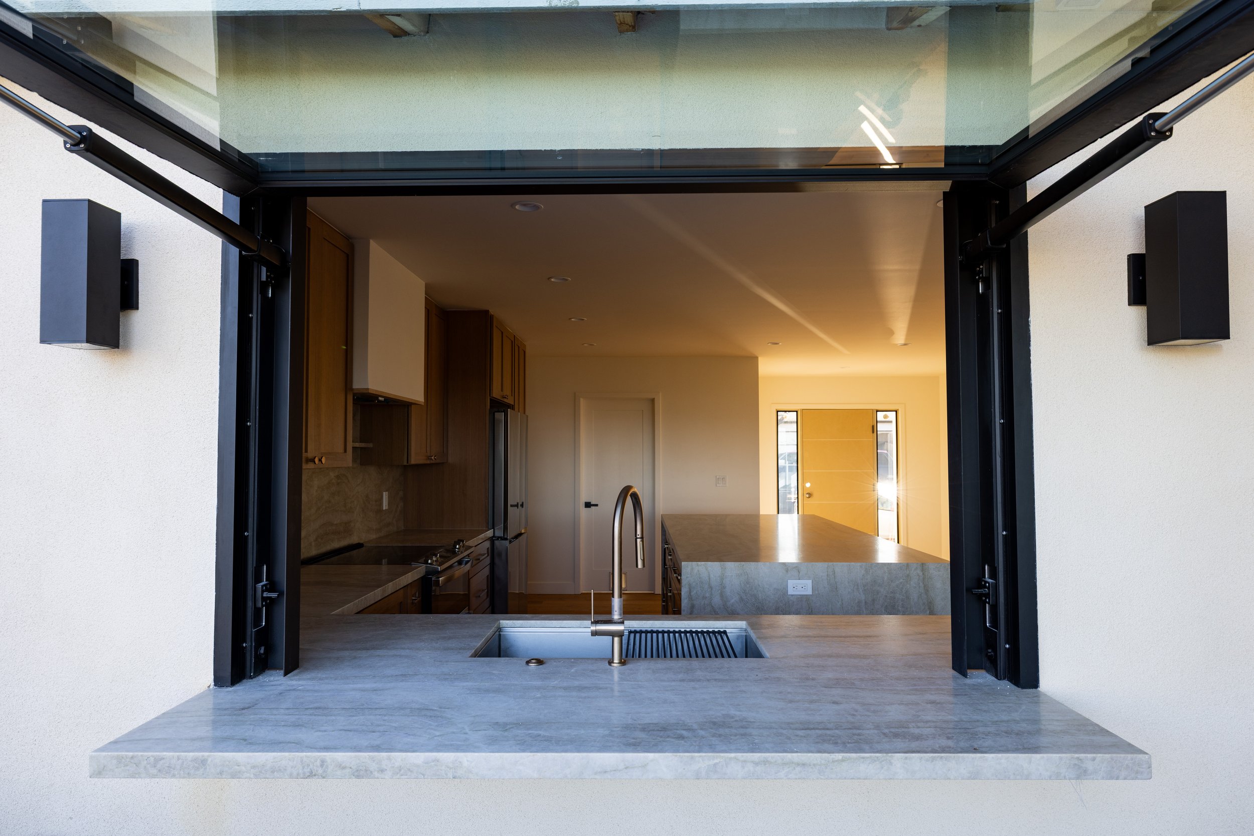 Image of the exterior of a newly remodeled home by Geis Architecture. Visible is the window which opens and closes above the kitchen couner which extends to the exterior for enjoying food and drinks both inside and outside