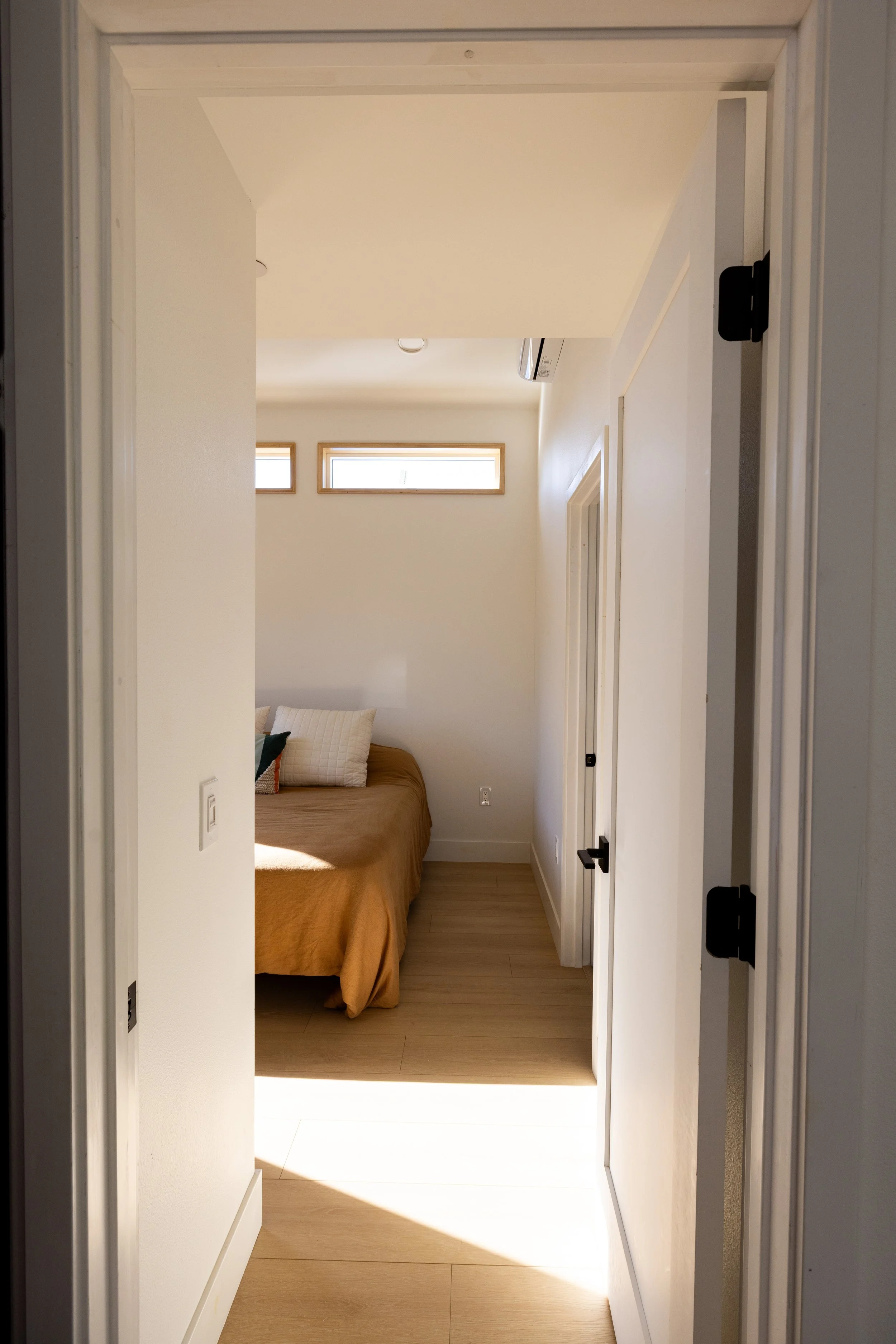 Modern clean entry to a brightly lit room with an earthy orange toned bed