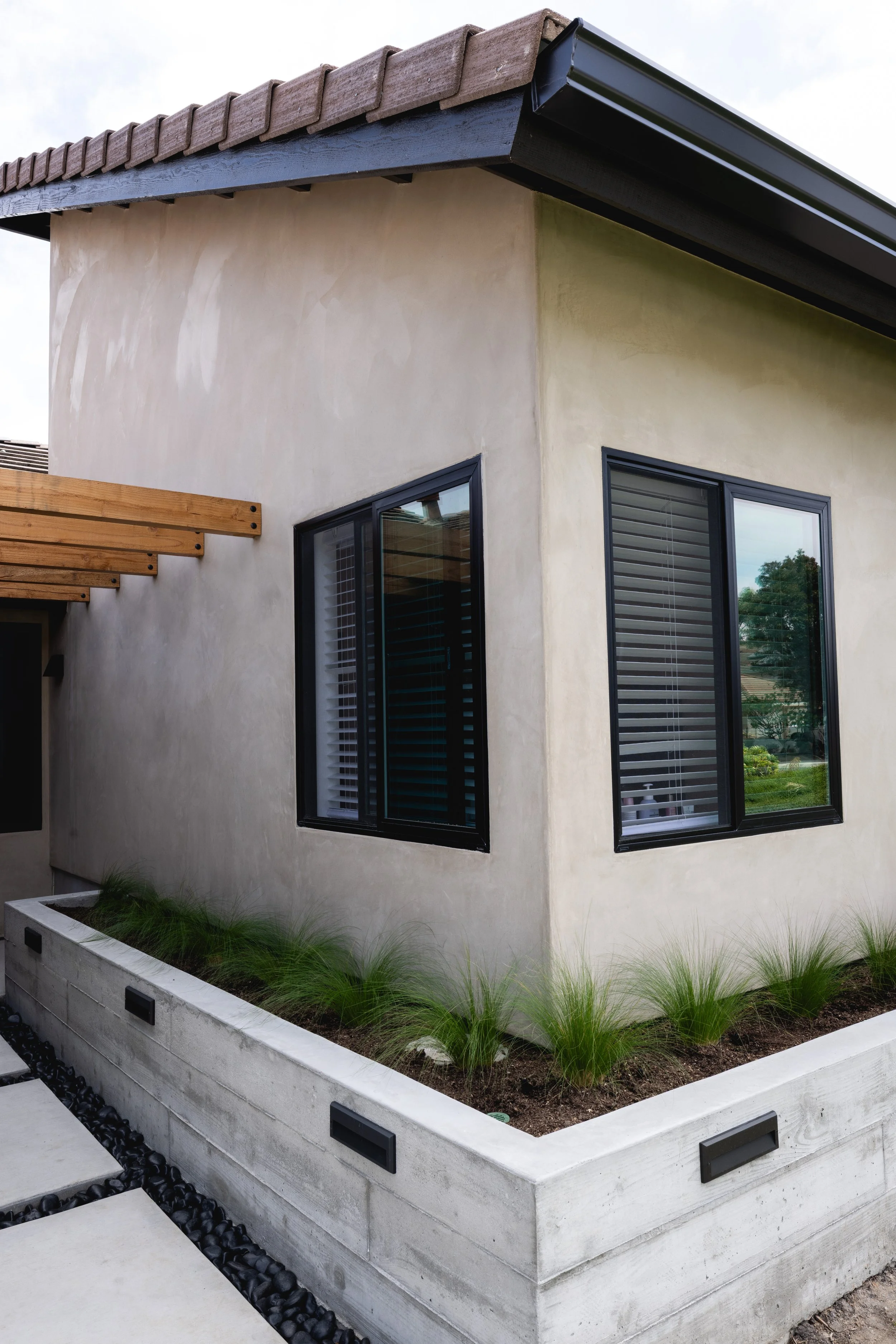 Displays new front addition on this Carlsbad home. Smooth stucco and black sleek modern windows and Mexican feather grass in concrete planter