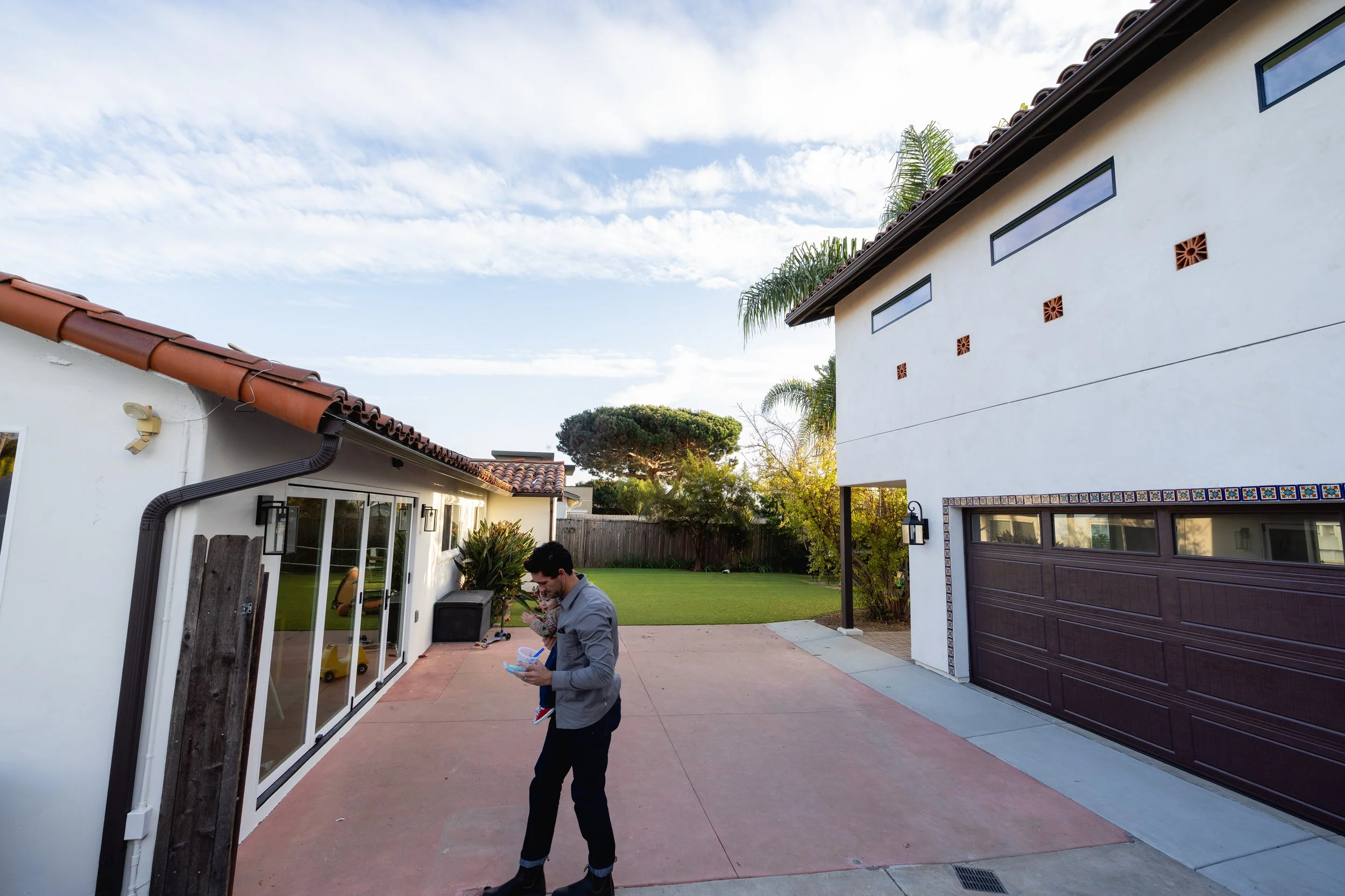 Man walking with child between main house and two story ADU. Spanish style, modern, family friendly casa designed by Geis Architecture