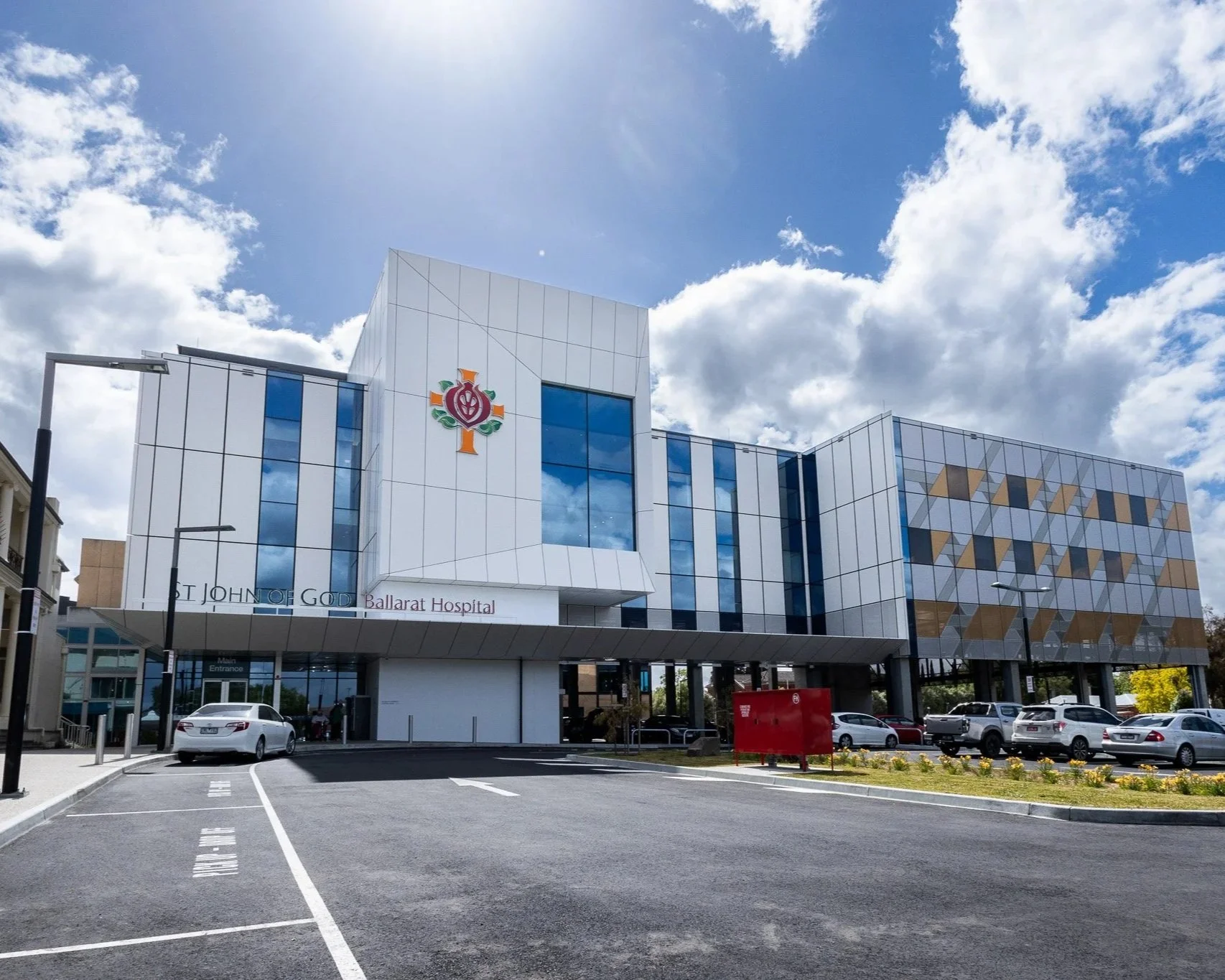Exterior of Ballarat Hospital building with parking lot in the foreground, blue sky with clouds above.