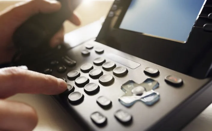 Close-up of a person's hand pressing buttons on a black office phone with a small screen.