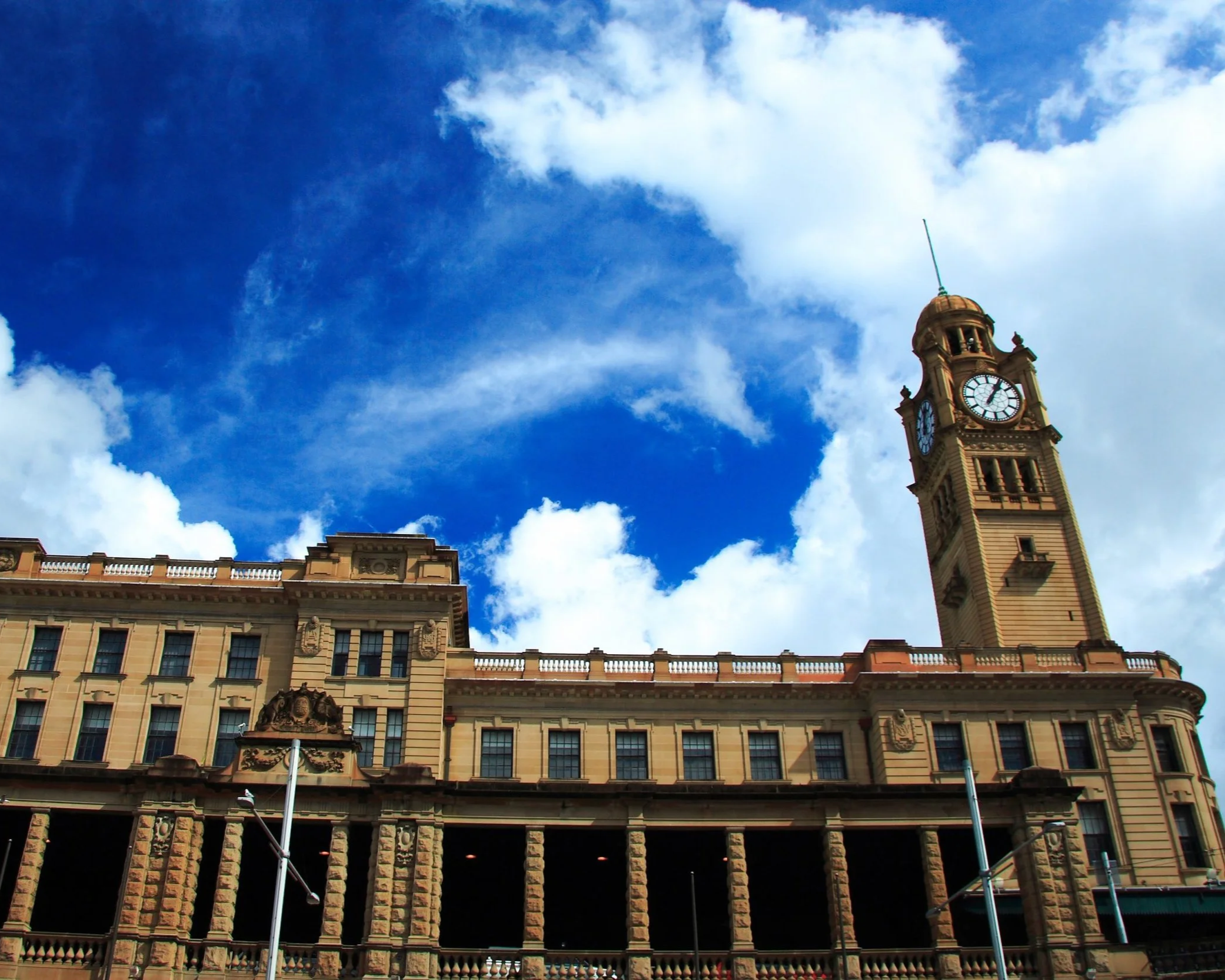 Historic city hall building with a tall clock tower under a partly cloudy blue sky.