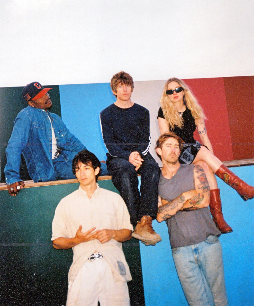 A five member band sitting in front of a multi-colored wall