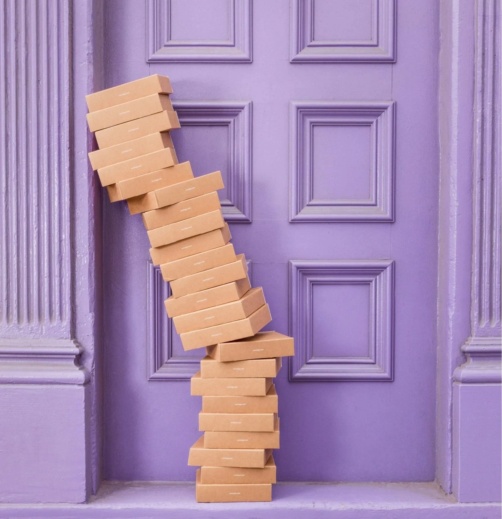 Stack of brown cardboard boxes leaning against a purple door with decorative molding.
