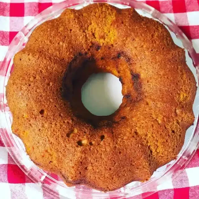 A golden brown Bundt cake in a glass dish on a red and white checkered tablecloth.