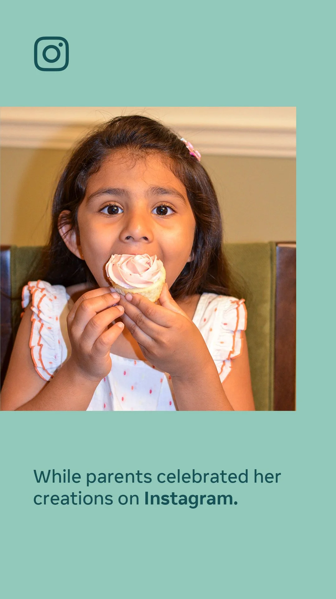 A young girl with dark hair and a pink hair clip eating a cupcake inside a restaurant.