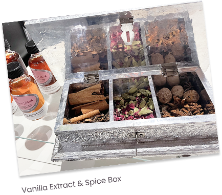 A decorative wooden box with a glass lid containing various dried spices, herbs, and potpourri, with bottles of essential oils on the side.