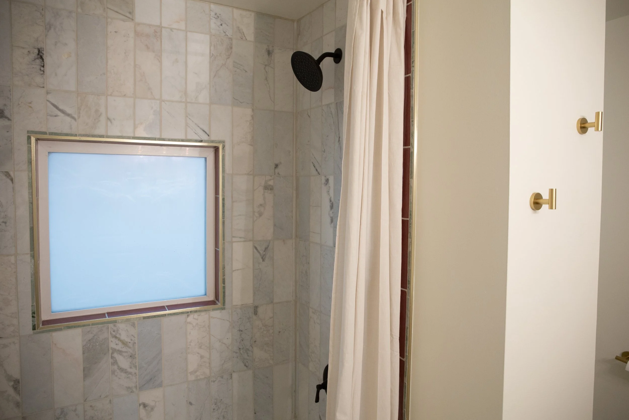 Shower with beige curtain, marble tile wall, black showerhead, frosted window.