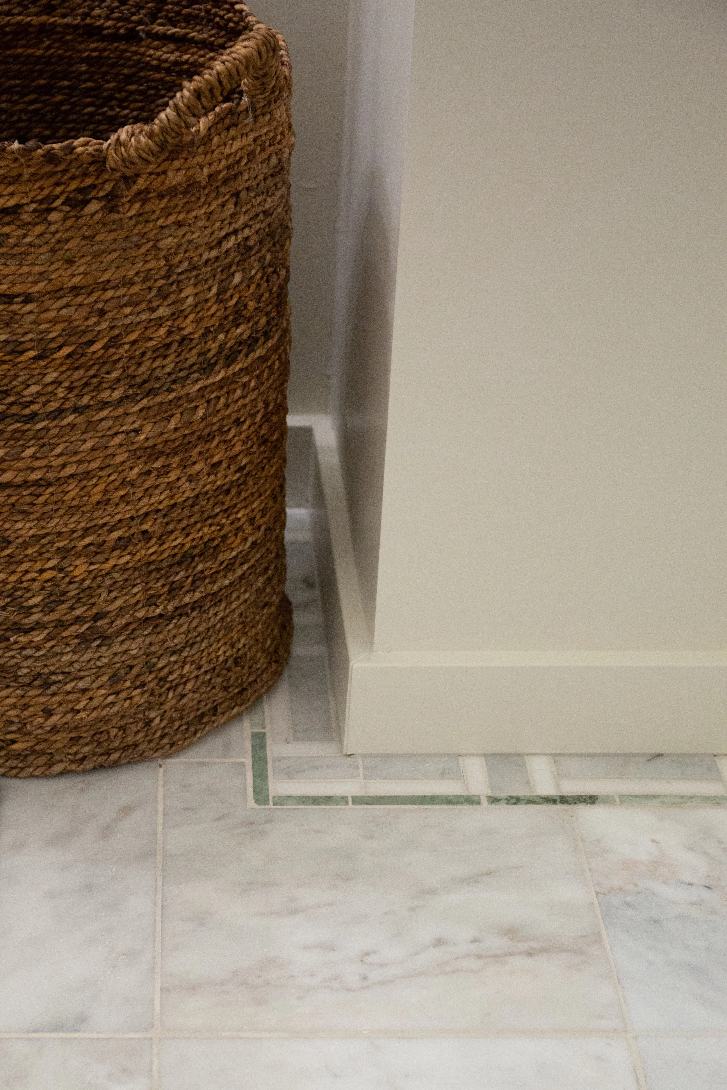 Close-up of a woven wicker basket next to a white cabinet on a tiled floor.