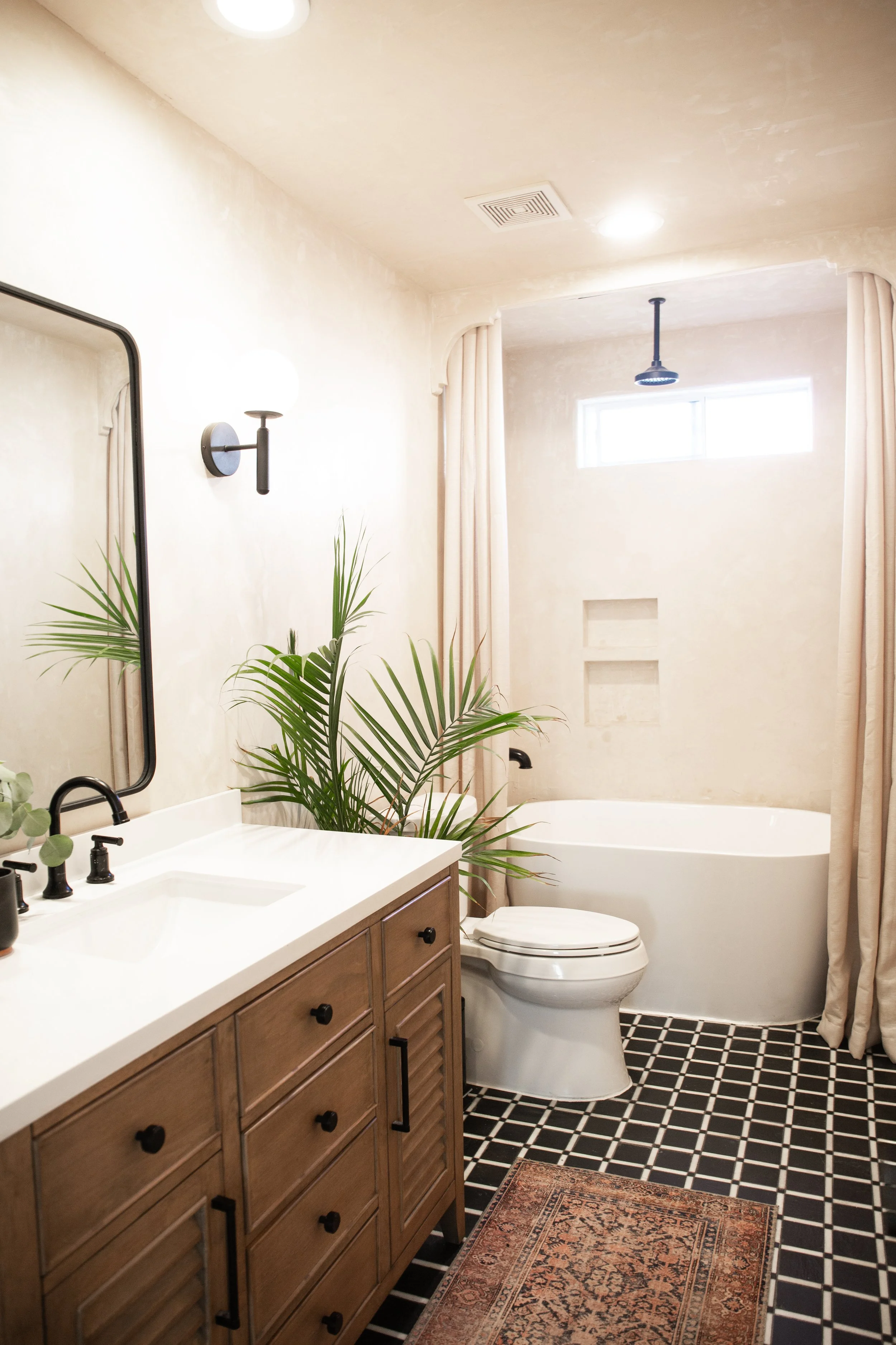 Modern bathroom with a wooden cabinet, black fixtures, a potted plant, a bathtub, toilet, window, and black and white checkered floor.