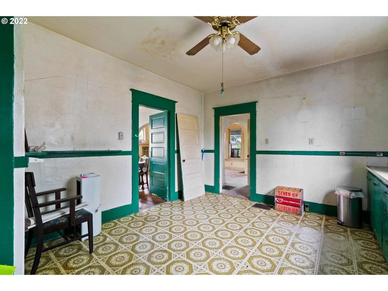Empty room with green door and trim, patterned linoleum floor, ceiling fan, and some clutter including a box and a chair.