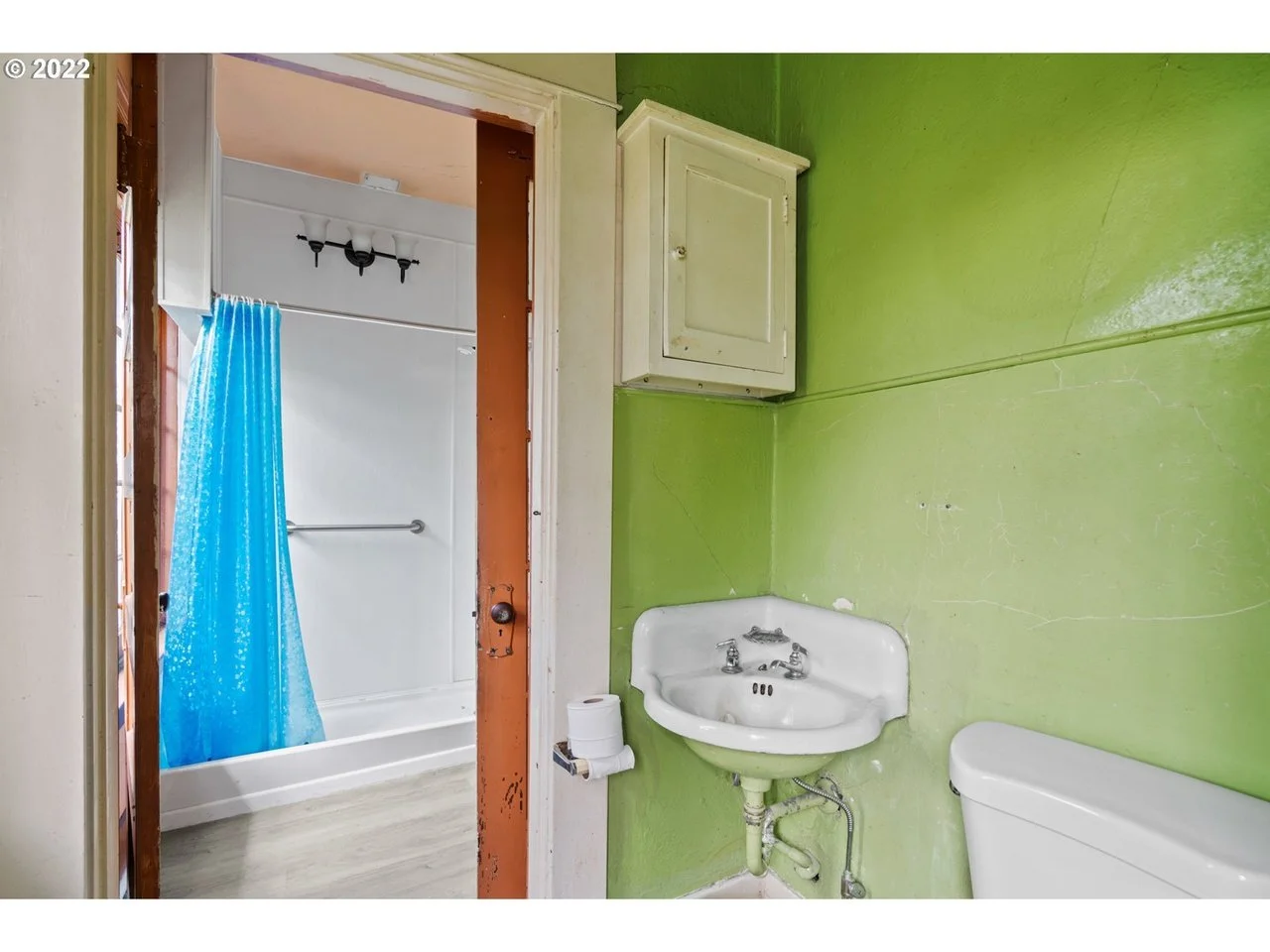 Small bathroom with green walls, a white sink, a toilet, a wall cabinet, and a view into a shower area with a blue shower curtain.
