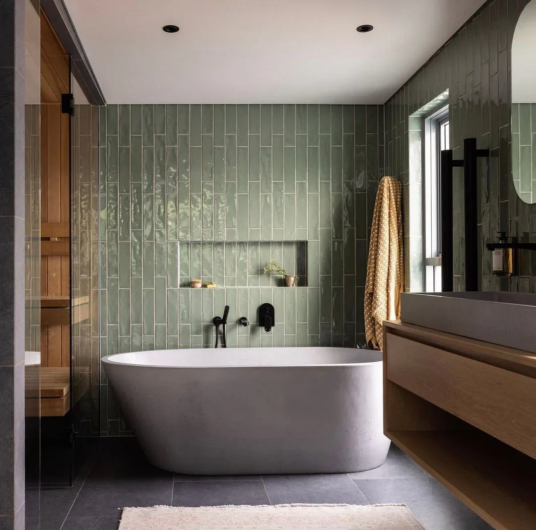 Modern bathroom with green tiled wall, freestanding bathtub, wooden vanity, and a window with a beige curtain.