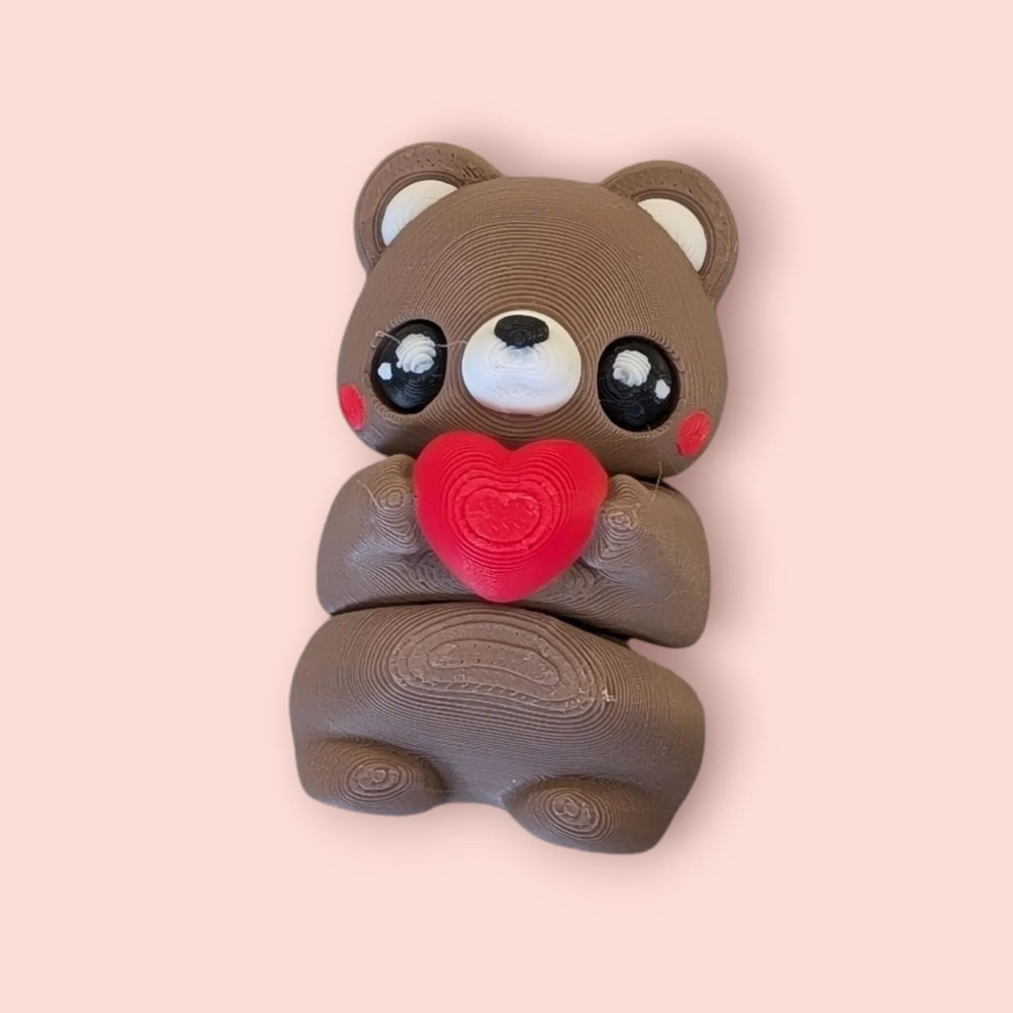 a 3d printed brown teddy bear with black eyes, holding a red heart. it has a flexi body and the ability to purchase a keychain for it