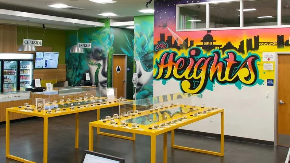 Indoor space with yellow display tables, graffiti art on the wall reading 'Heights', and signs for curbside and express services.